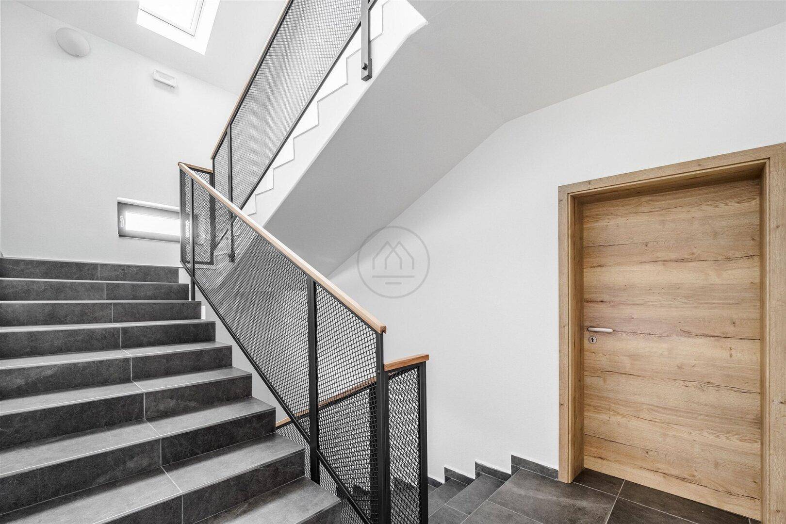 Treppenhaus mit modernen Fliesenstufen und Metallgeländer.