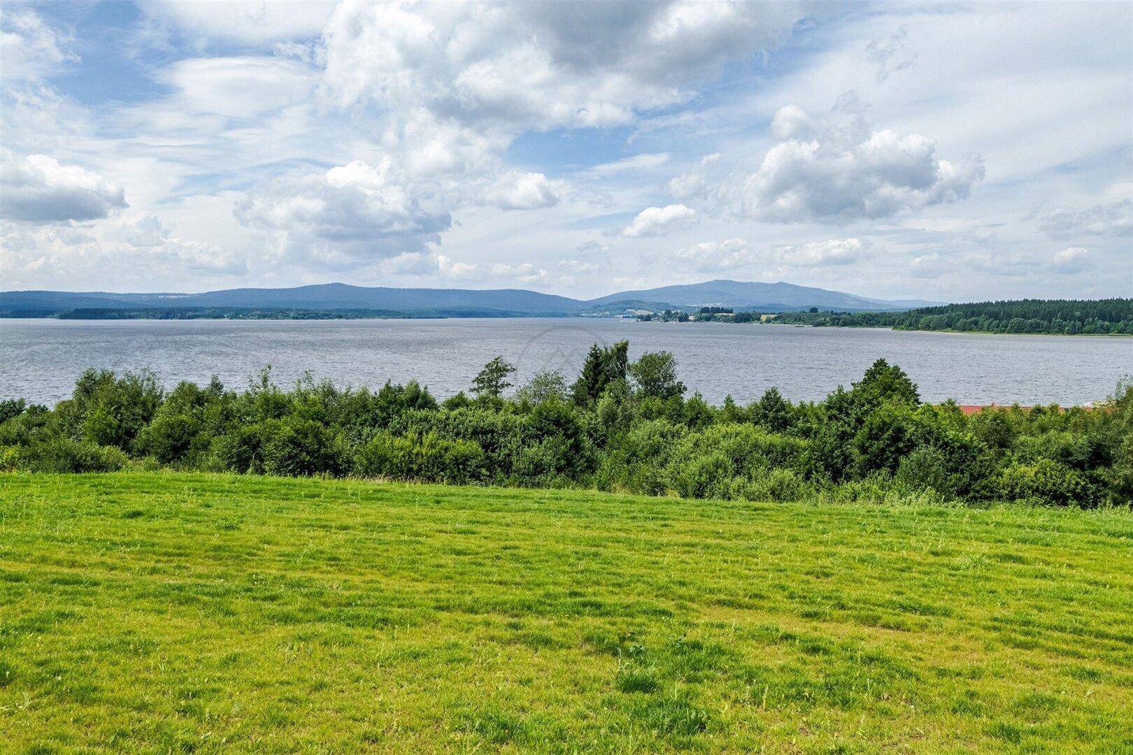 Weitläufige grüne Landschaft mit See und Bergen im Hintergrund.