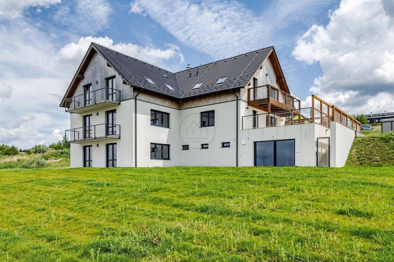 Modernes Haus mit mehreren Balkonen und Terrassen in grüner Umgebung.