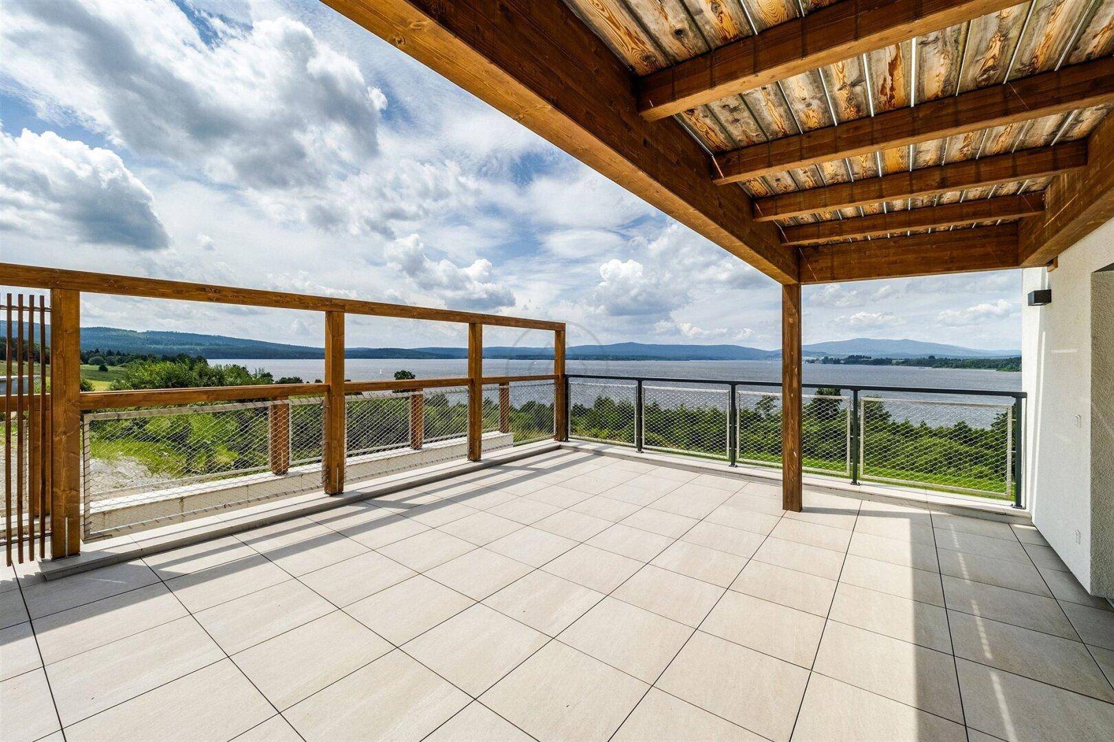 Geräumige überdachte Terrasse mit Fliesenboden und Panoramablick auf den See.