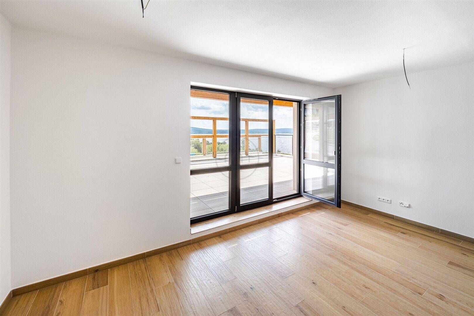 Lichtdurchfluteter Raum mit Holzboden und großem Fenster mit Terrassenzugang.