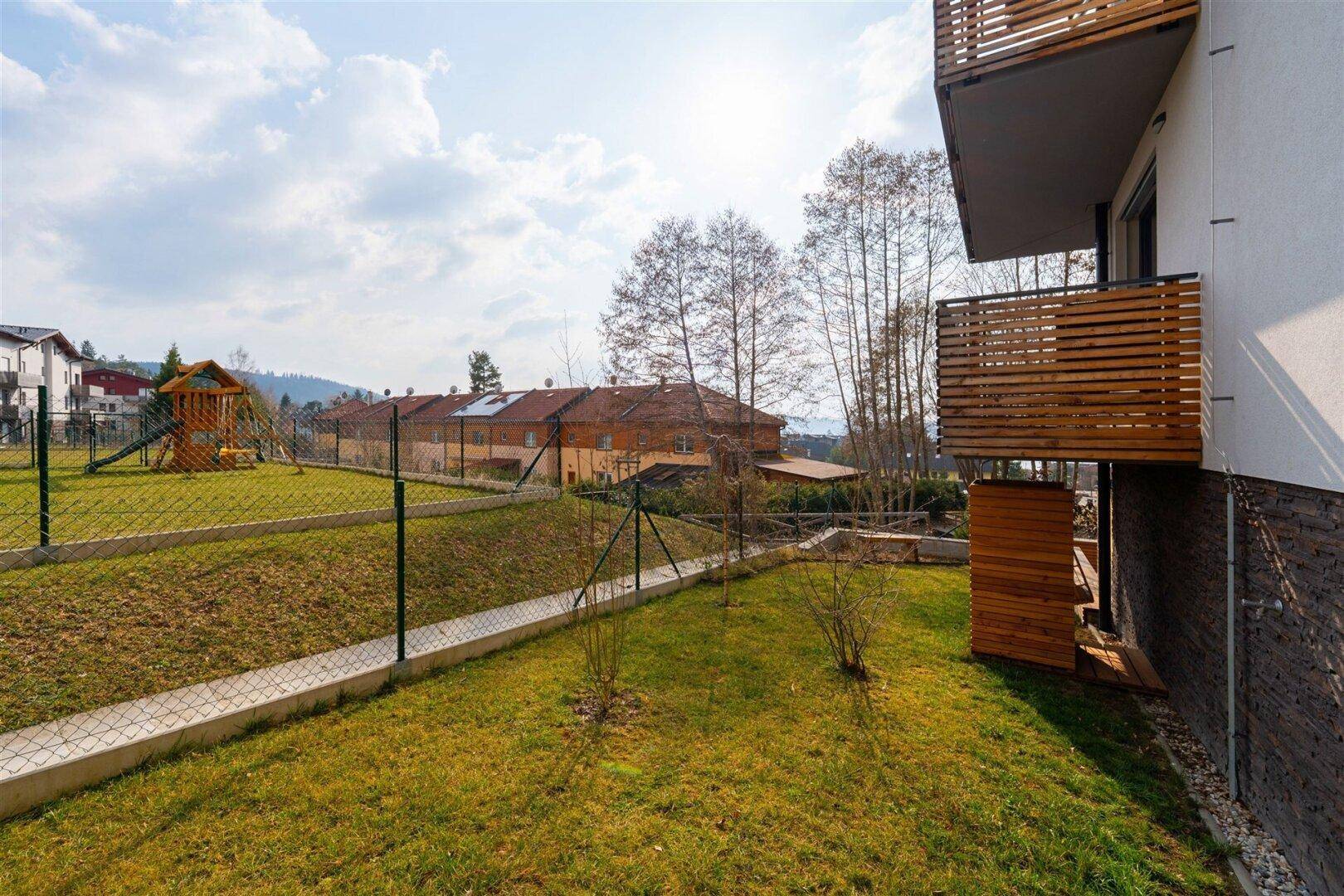 Weitläufige Grünfläche neben dem Gebäude mit Blick auf den Spielplatz und die Umgebung.