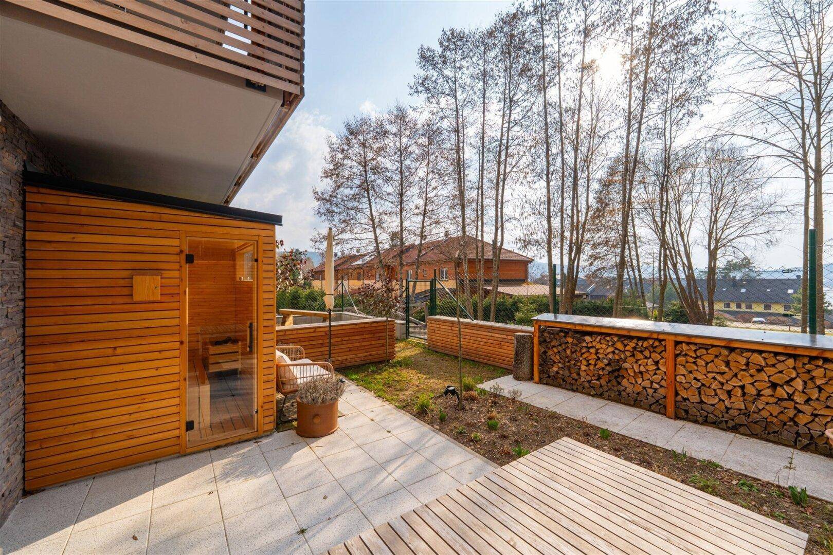 Sonniger Außenbereich mit Terrasse, Sauna und Blick auf die umliegende Natur.