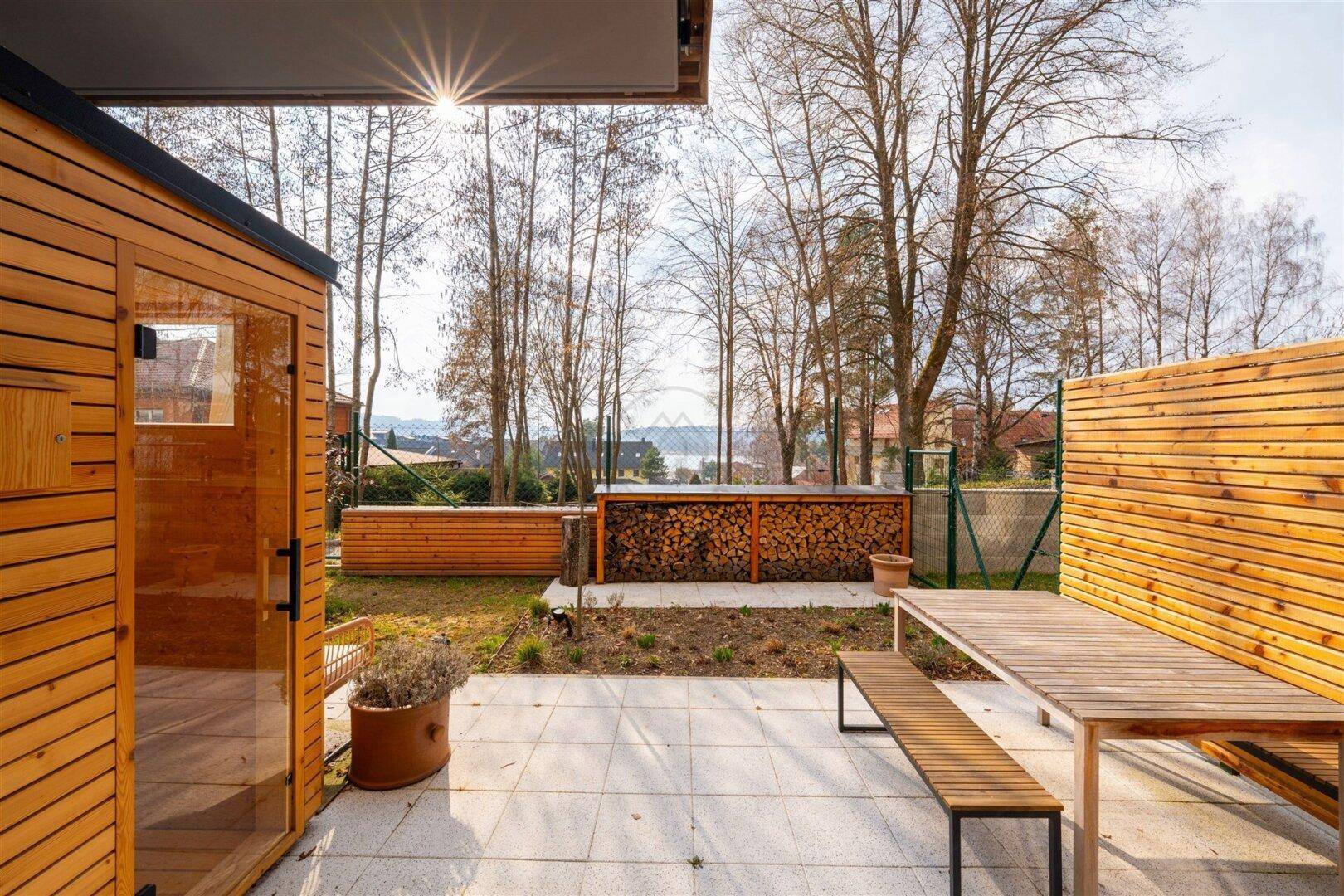 Sonniger Terrassenbereich mit Esstisch, Bänken und Blick auf den See im Hintergrund.