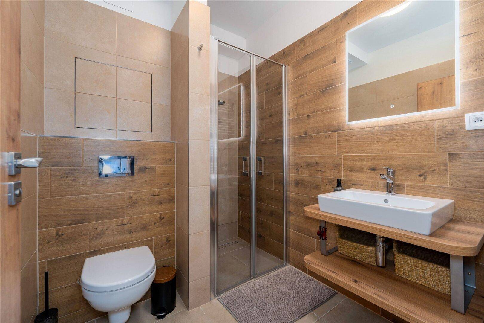 Modernes Badezimmer mit Holzoptikfliesen, Duschkabine und wandhängendem WC.