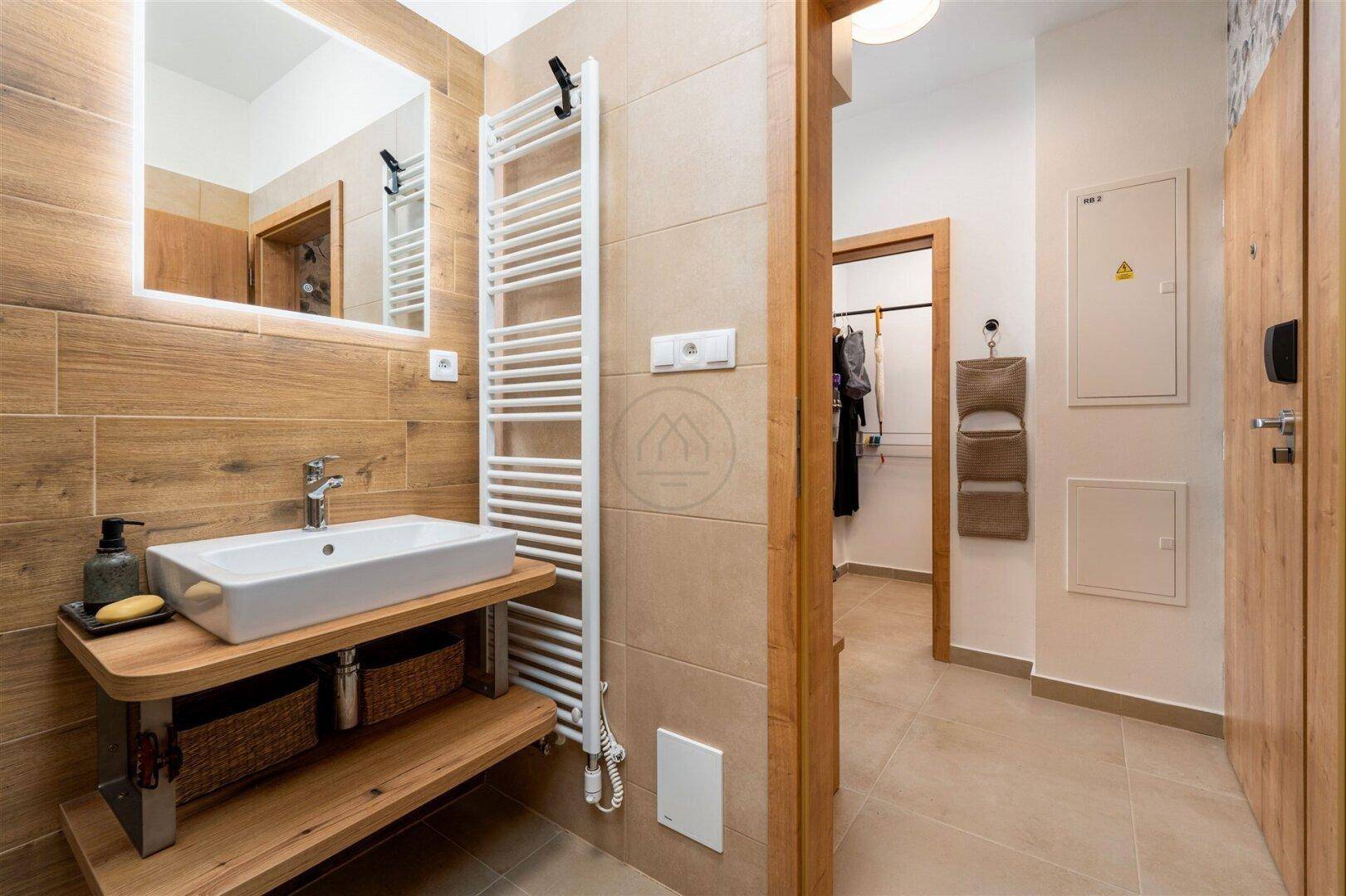 Helles Badezimmer mit Holzoptikfliesen, Waschtisch und beheiztem Handtuchhalter.