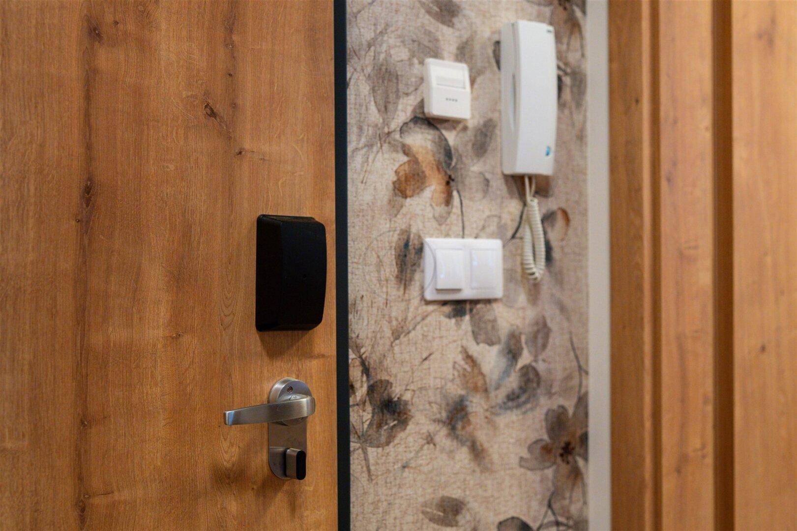 Eingangsbereich mit Holztür, Gegensprechanlage und floraler Tapete an der Wand.