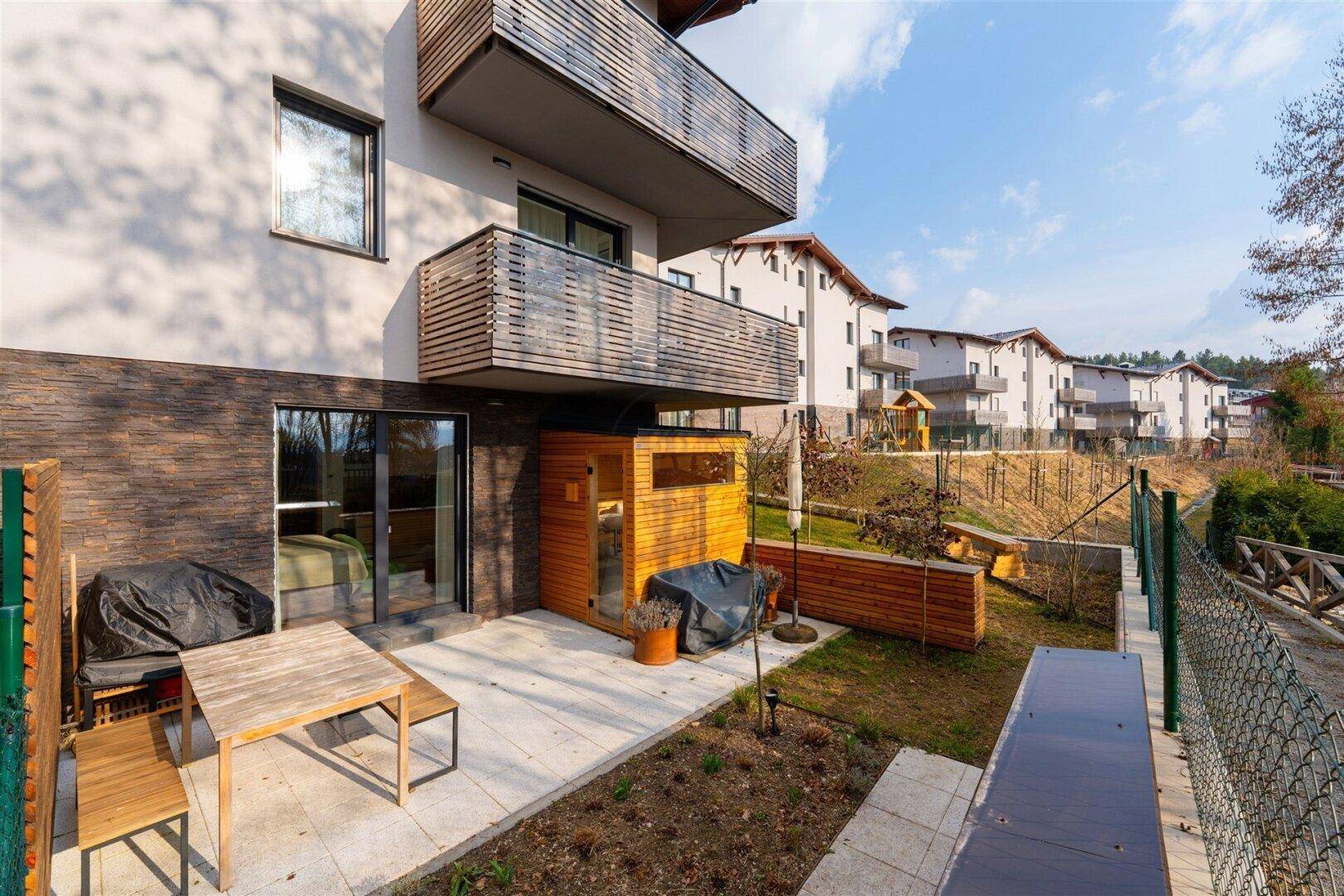 Terrasse mit Gartenmöbeln, Sauna und Blick auf die Wohnanlage und den Spielplatz.