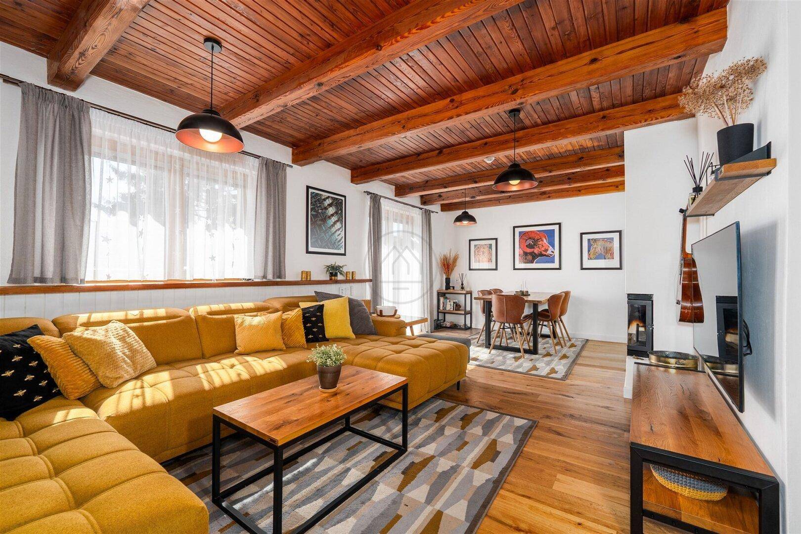 Gemütlicher offener Wohn-Essbereich mit Holzbalkendecke, gelbem Sofa und Holzboden.