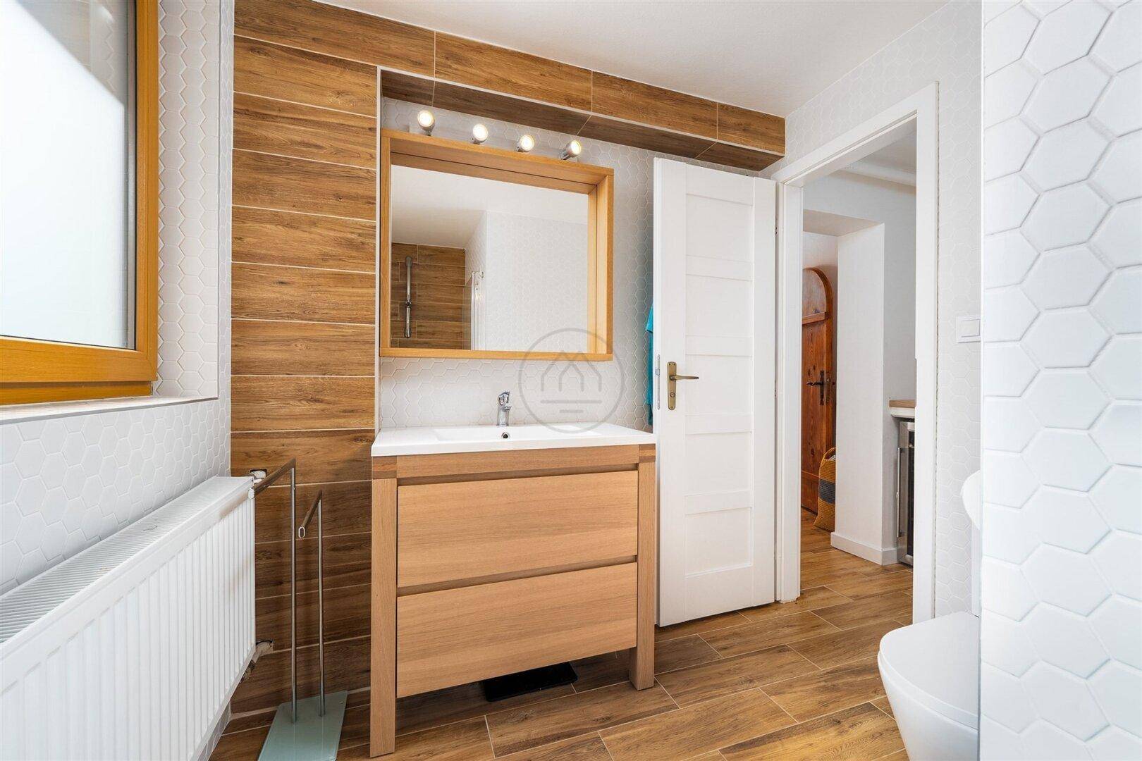 Helles Badezimmer mit Holzwaschtisch, Spiegel und modernen Fliesen in Holzoptik.