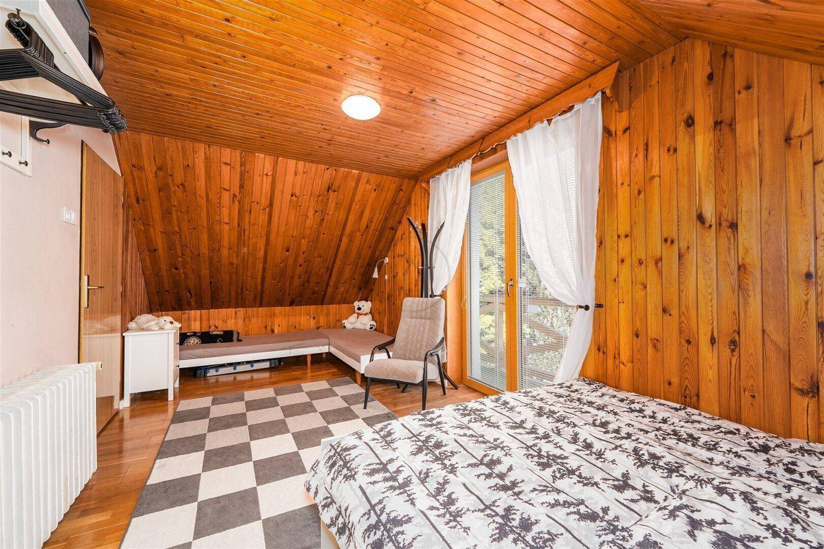 Schlafzimmer im Dachgeschoss mit Holzwänden, Holzbalkendecke und Zugang zum Balkon.
