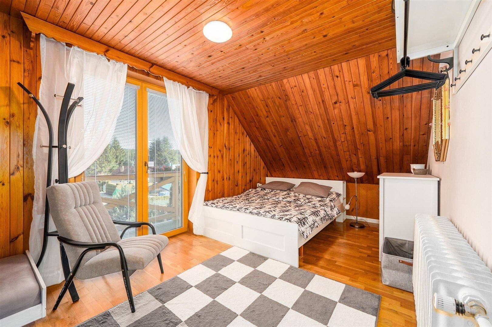 Helles Schlafzimmer im Dachgeschoss mit Holzwänden, Holzbalkendecke und Balkonzugang.
