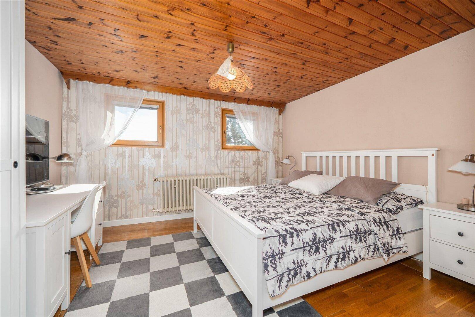 Geräumiges Schlafzimmer mit Holzbalkendecke, Doppelbett und Schreibtisch.