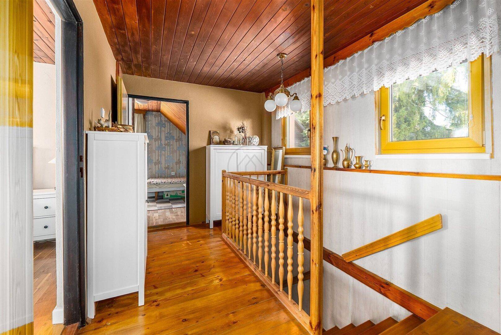 Heller Flur im Obergeschoss mit Holzgeländer, Holzboden und Fenster.