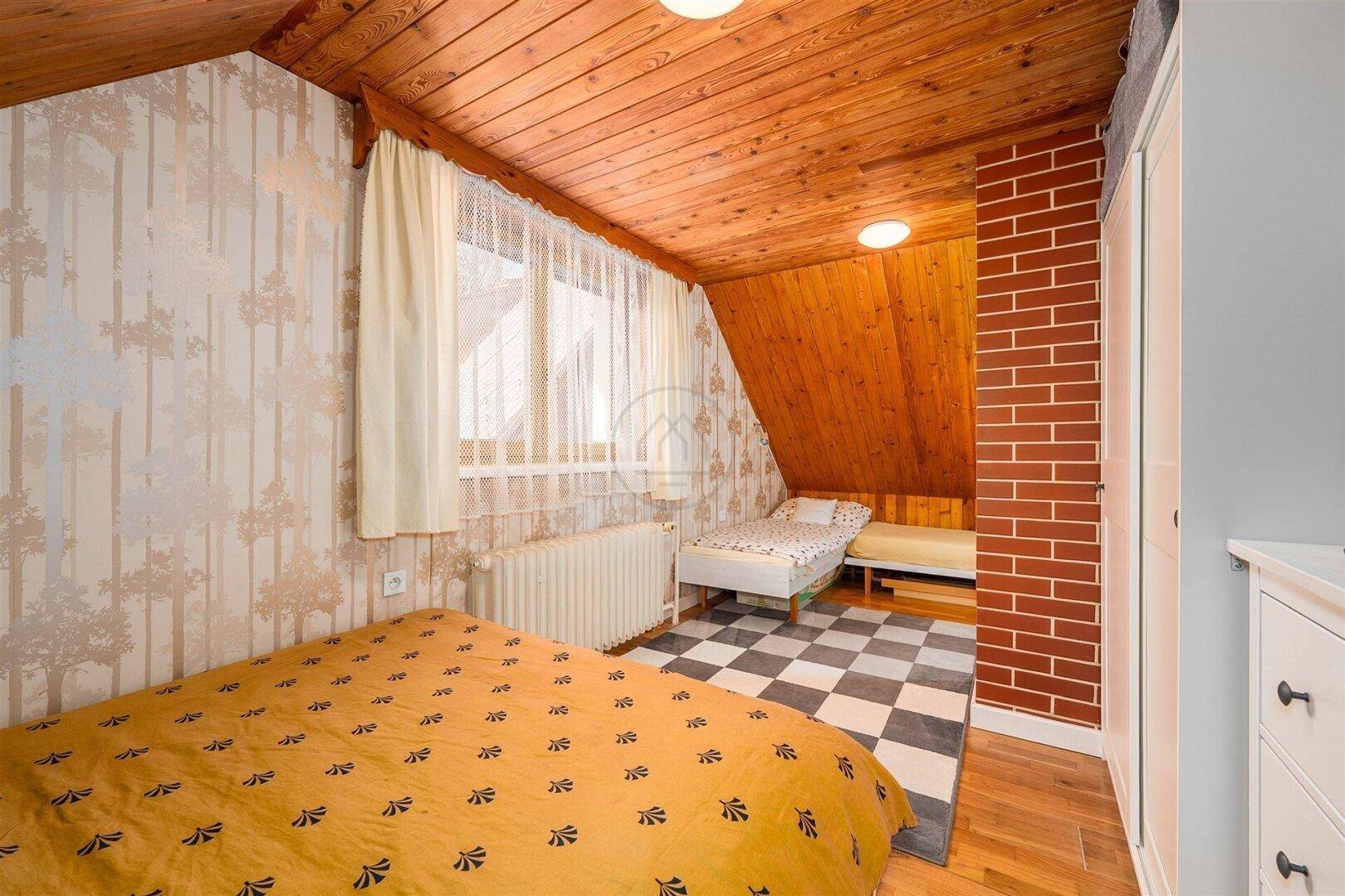 Helles Schlafzimmer im Dachgeschoss mit Holzbalkendecke, Fenster und gemusterter Tapete.