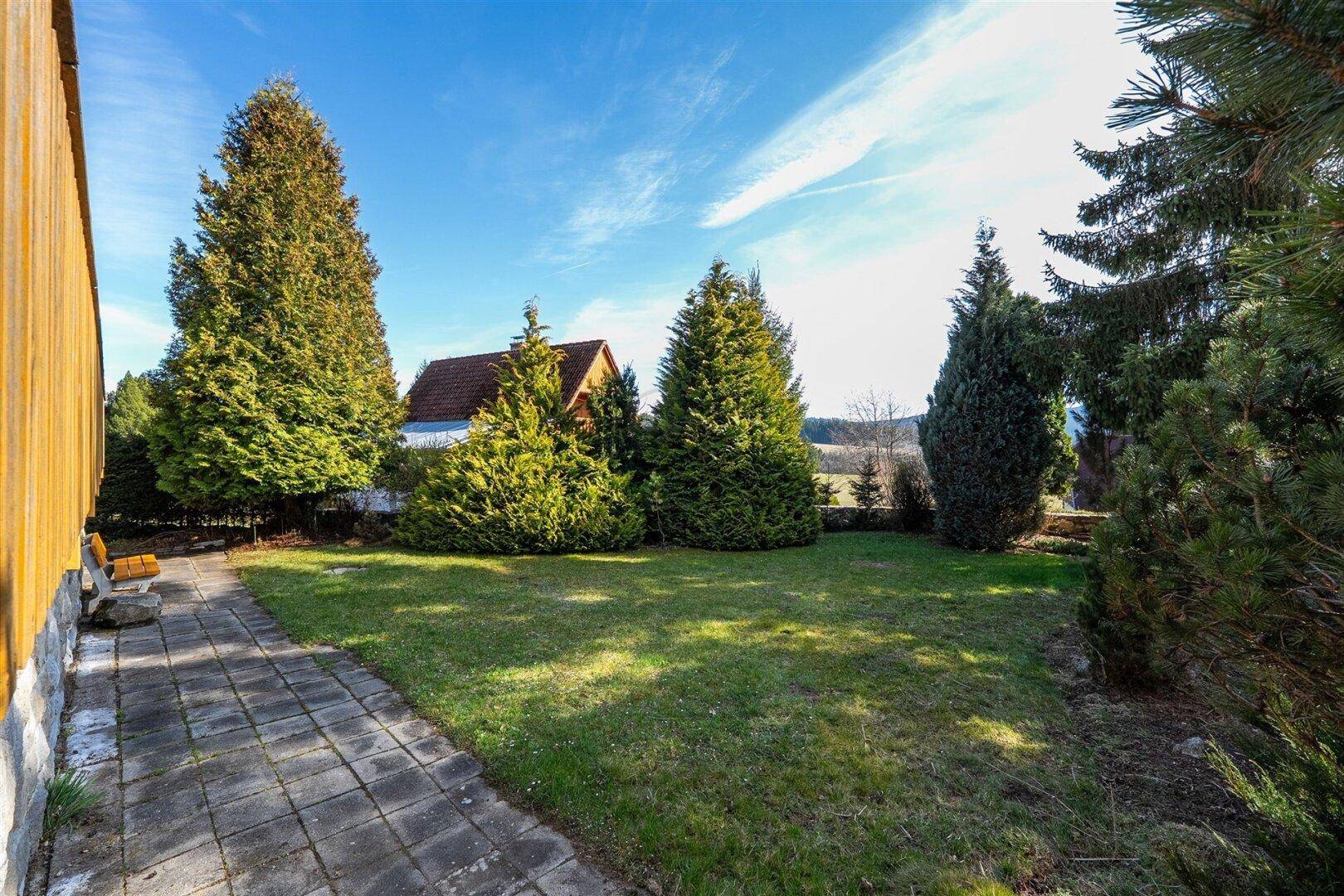 Gepflegter Gartenbereich mit Rasenfläche und hohen Bäumen neben dem Haus.