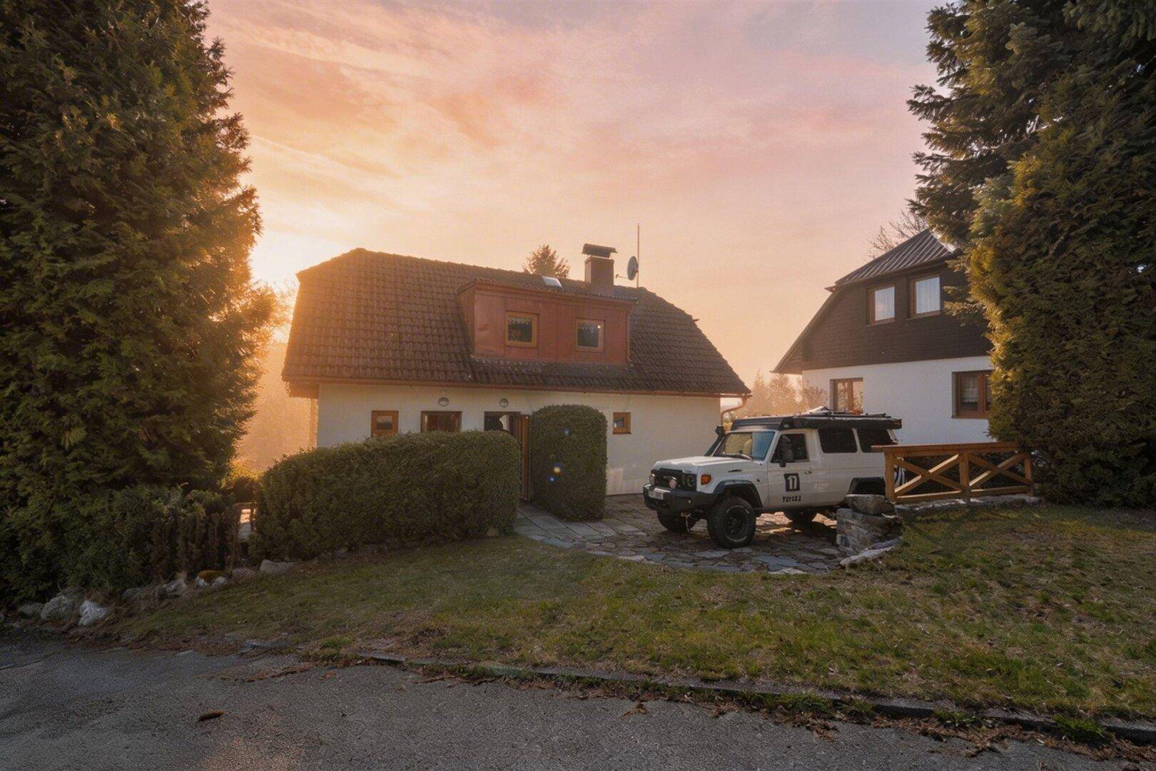 Hausfassade bei Sonnenuntergang mit Einfahrt und geparktem Geländewagen.