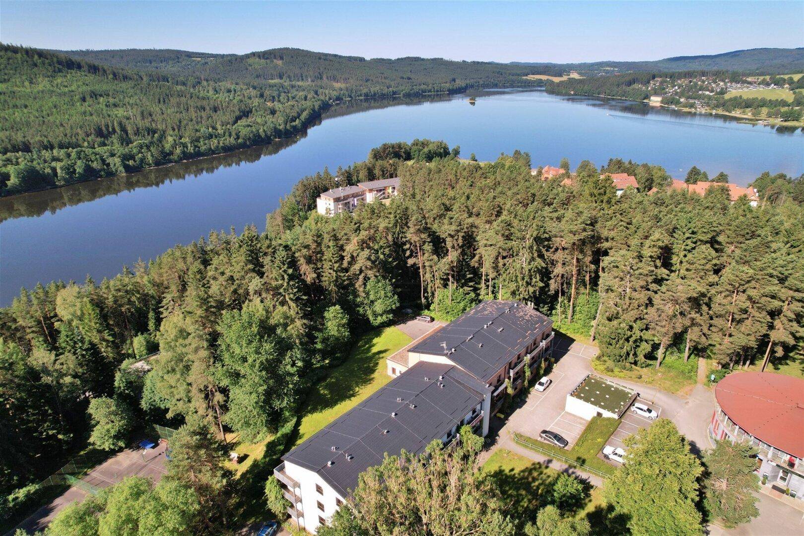 Luftaufnahme der Wohngebäude in waldreicher Umgebung mit weitem Blick auf den See.