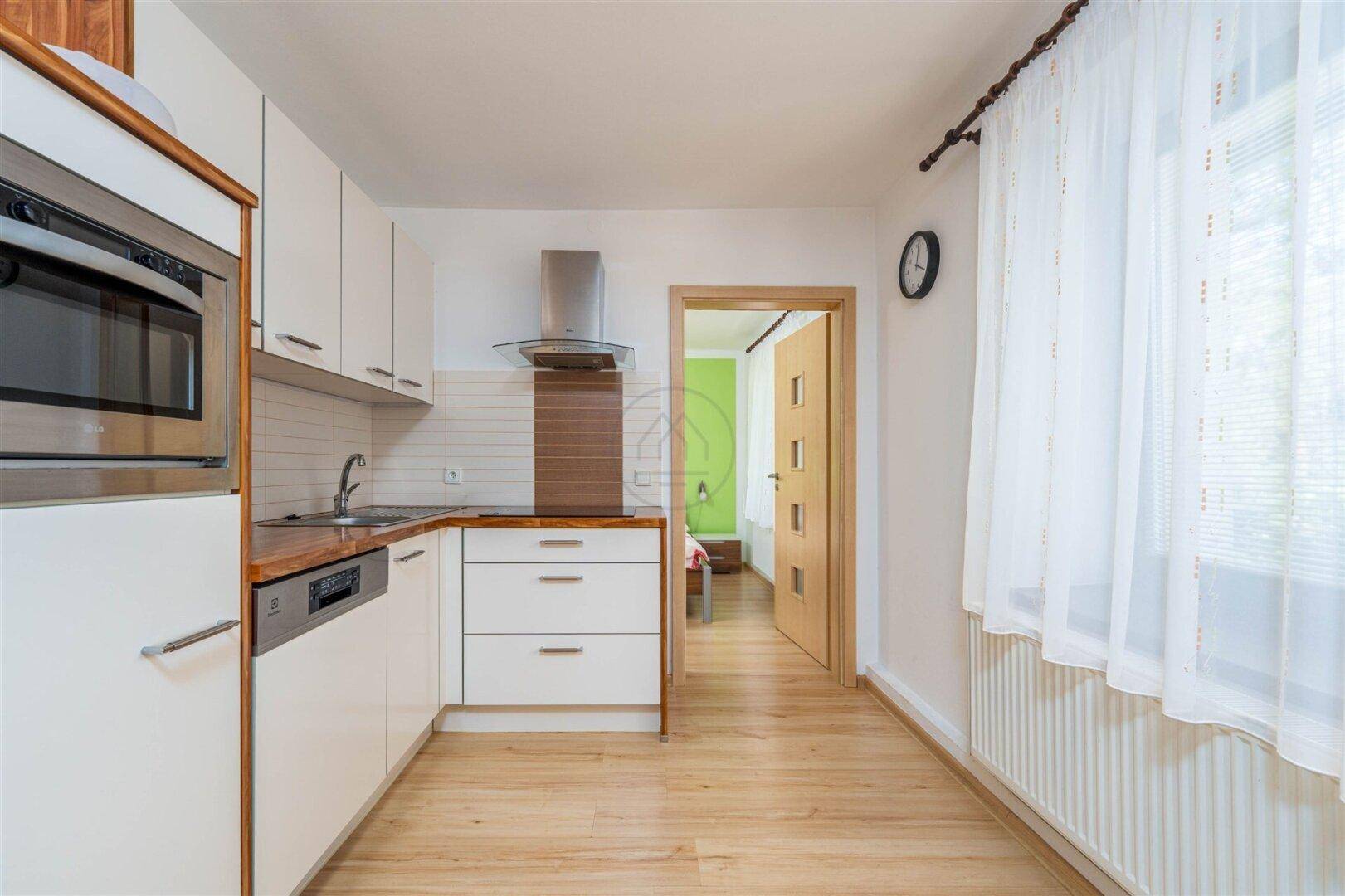 Funktionale Küche mit weißen Schränken, Holzarbeitsplatte und Blick in ein Schlafzimmer.