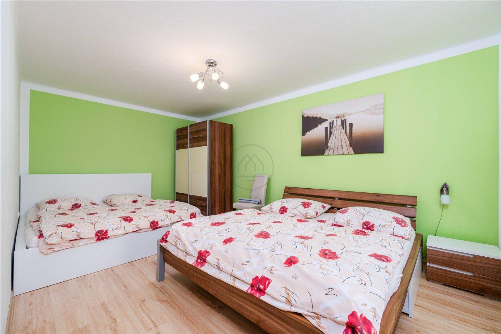 Helles Schlafzimmer mit zwei Betten, grünen Wänden und Holzmöbeln.