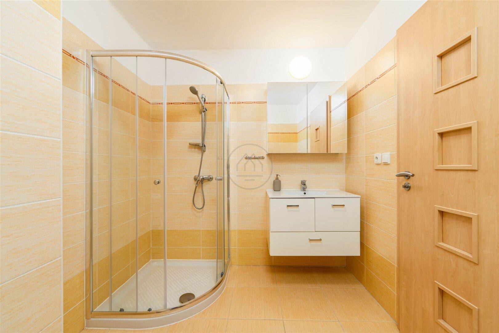 Modernes Badezimmer mit Duschkabine, Waschtisch und hellen Fliesen an Wänden und Boden.