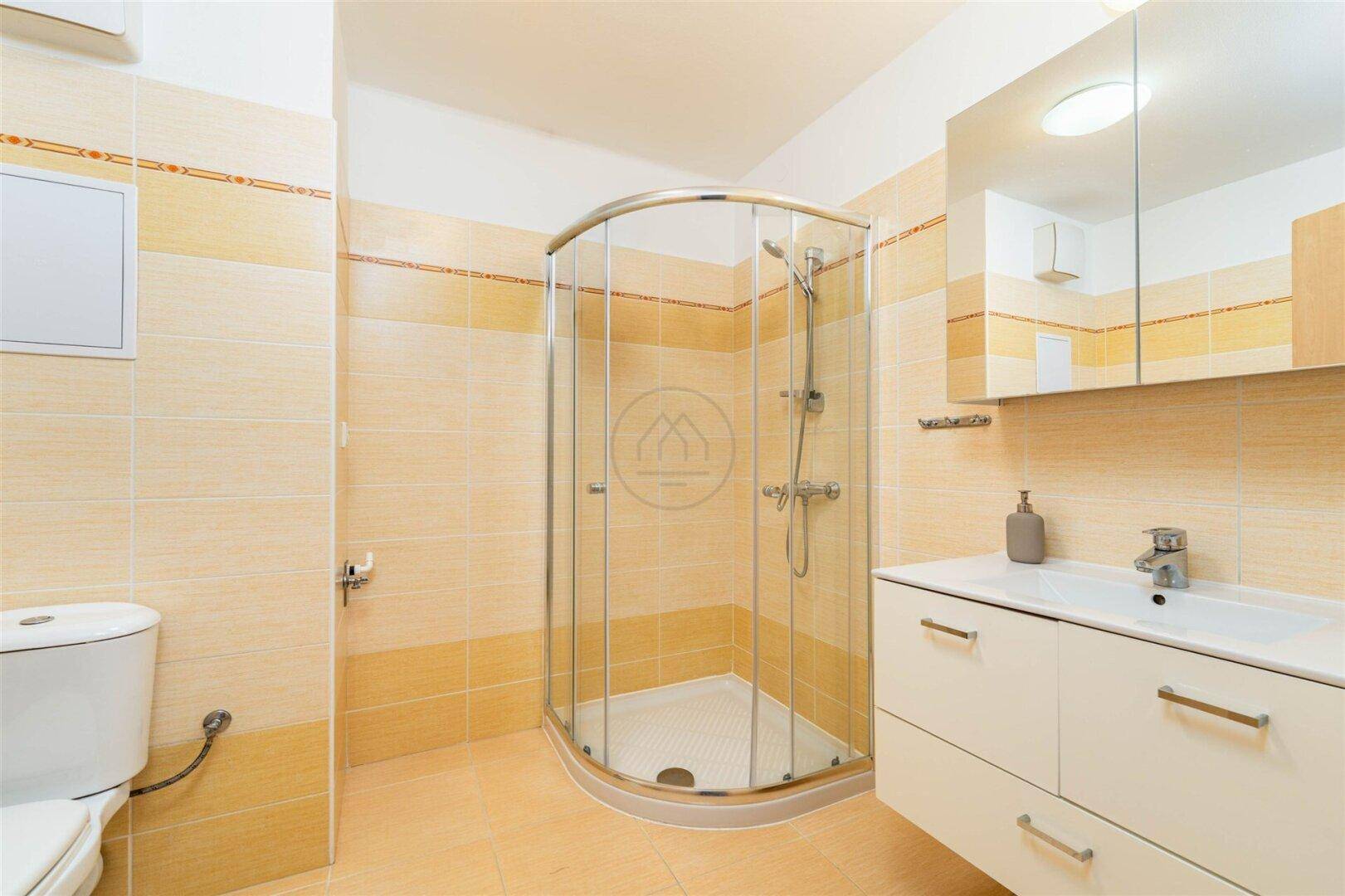 Badezimmer mit Duschkabine, Toilette und Waschtisch, ausgestattet mit hellen Fliesen.