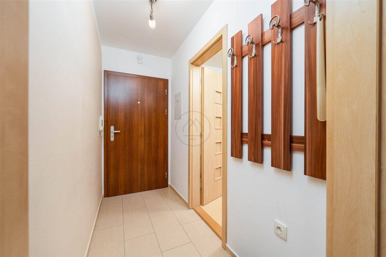 Heller Flur mit Fliesenboden, Garderobe und Holztüren zu den angrenzenden Räumen.