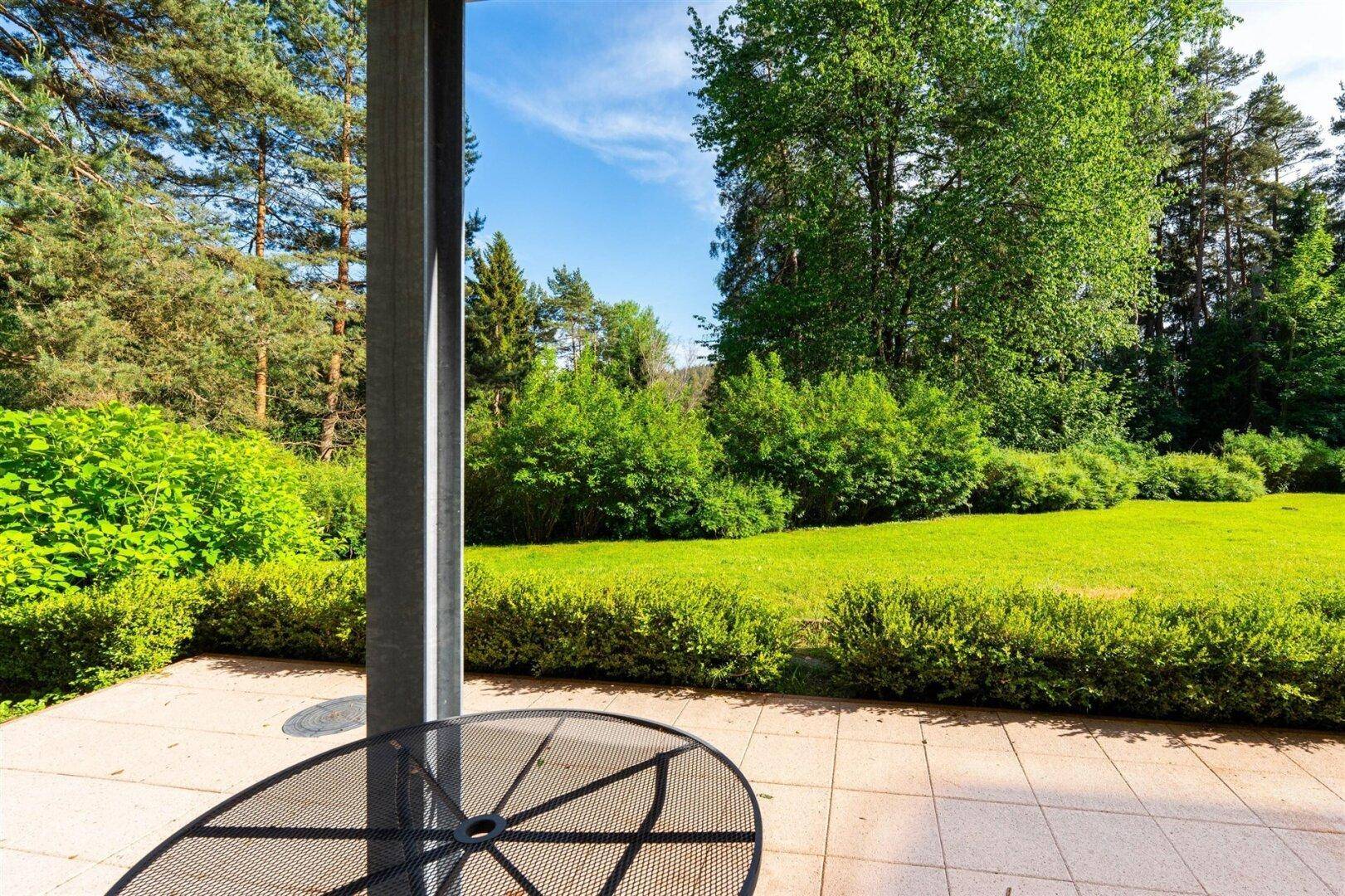 Ruhige Terrasse mit Blick auf die weitläufige Grünfläche und den umgebenden Baumbestand.