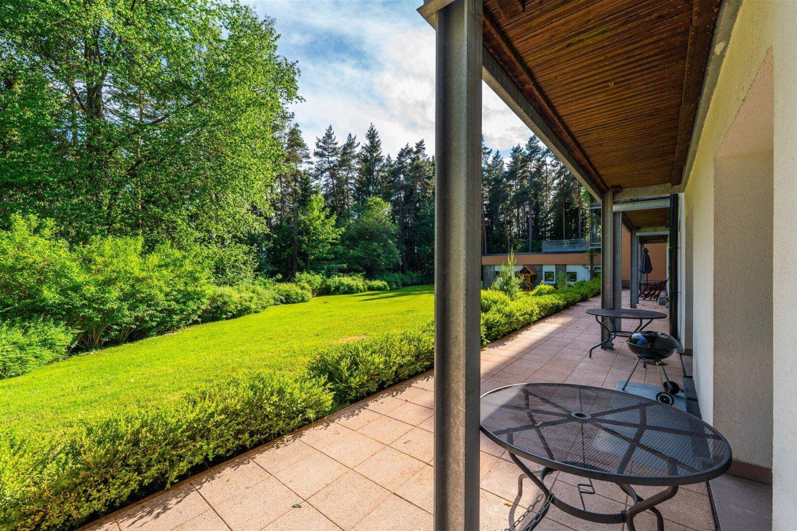 Geräumige Terrasse mit Grill und Blick auf die gepflegte Rasenfläche und den Waldrand.