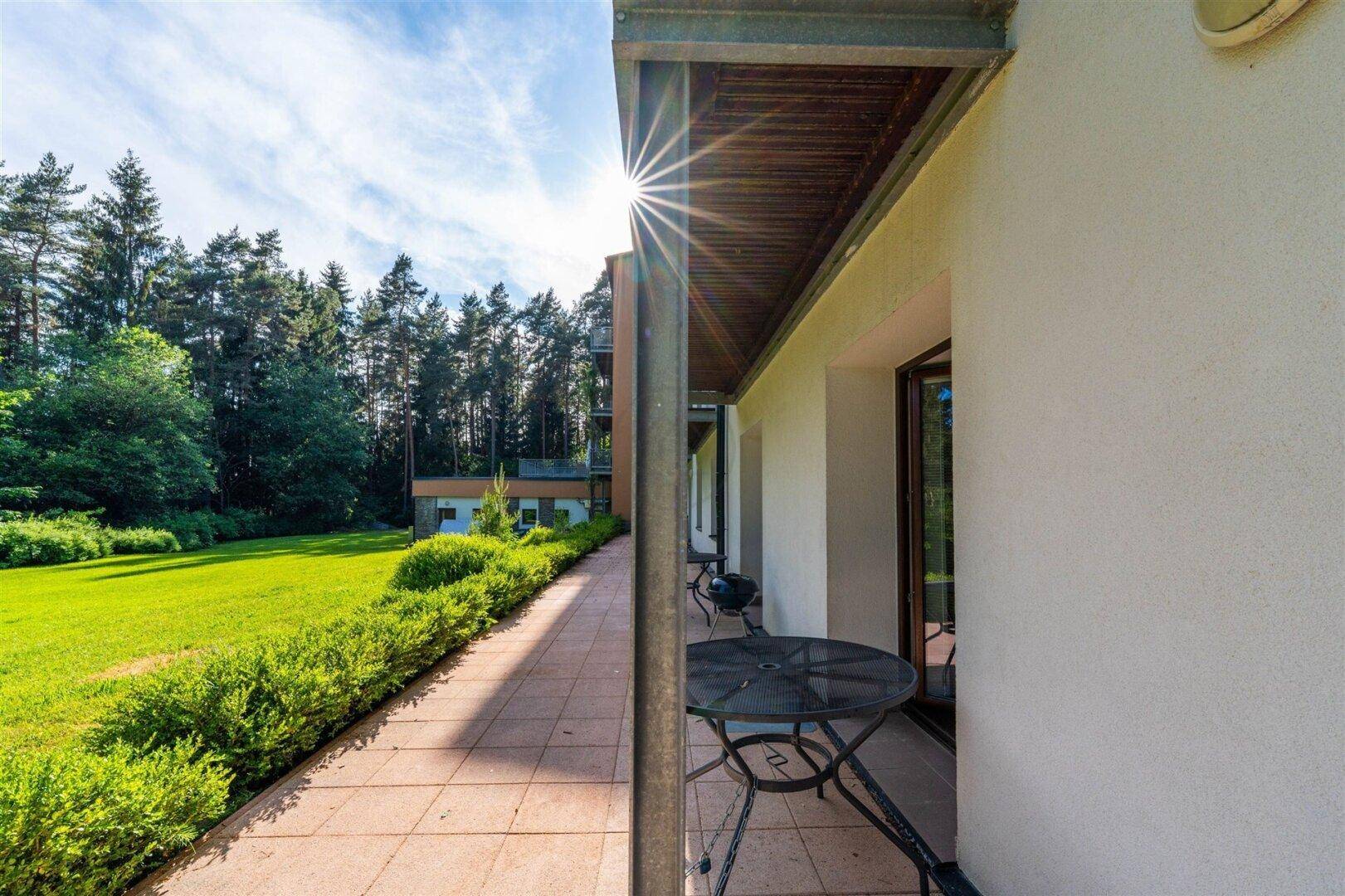 Sonniger Terrassenbereich mit Gartenmöbeln und weitem Blick auf die grüne Wiese und Bäume.
