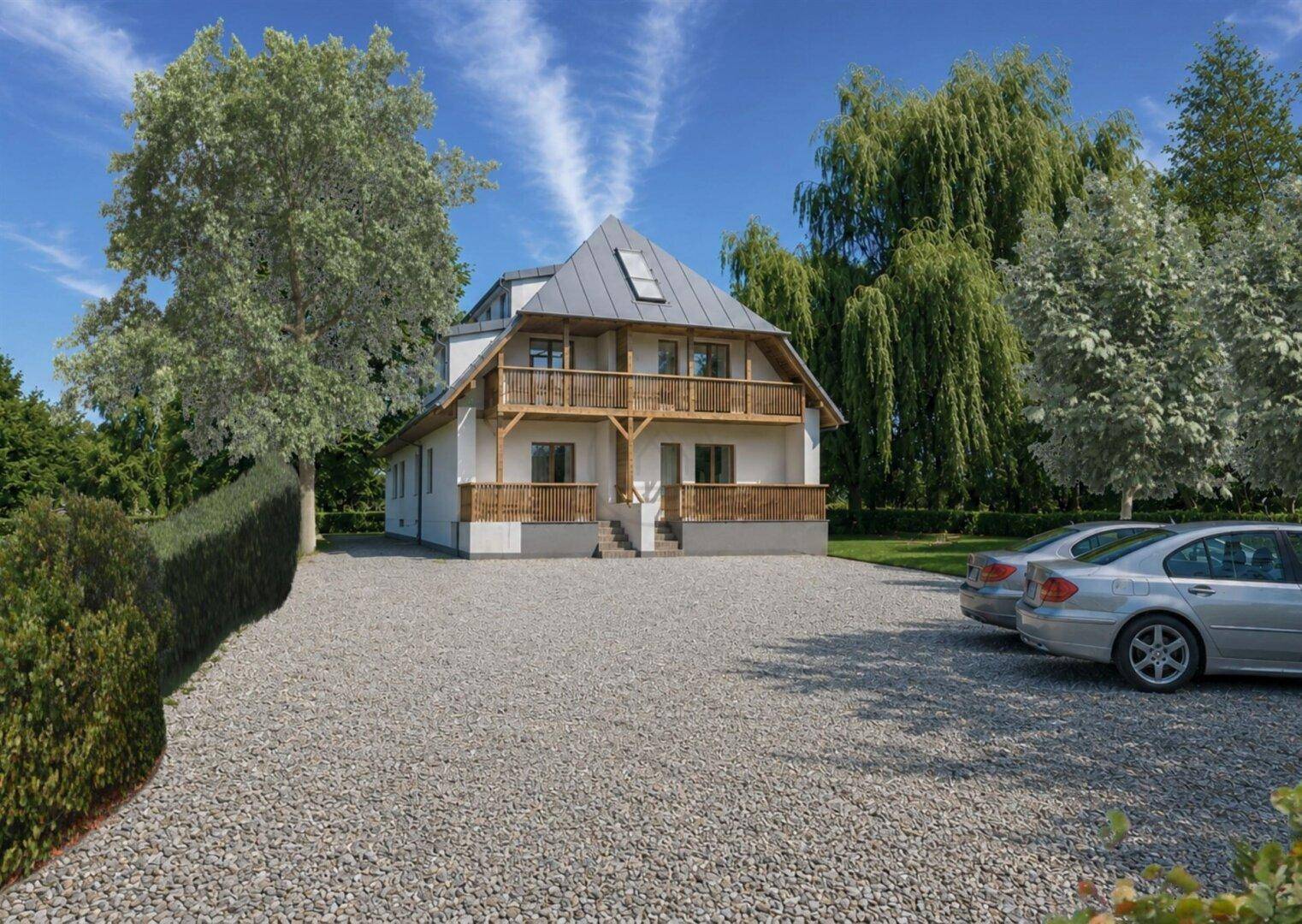 Modernes Gebäude mit Satteldach, Holzdetails und Schotterparkplatz in grüner Umgebung.