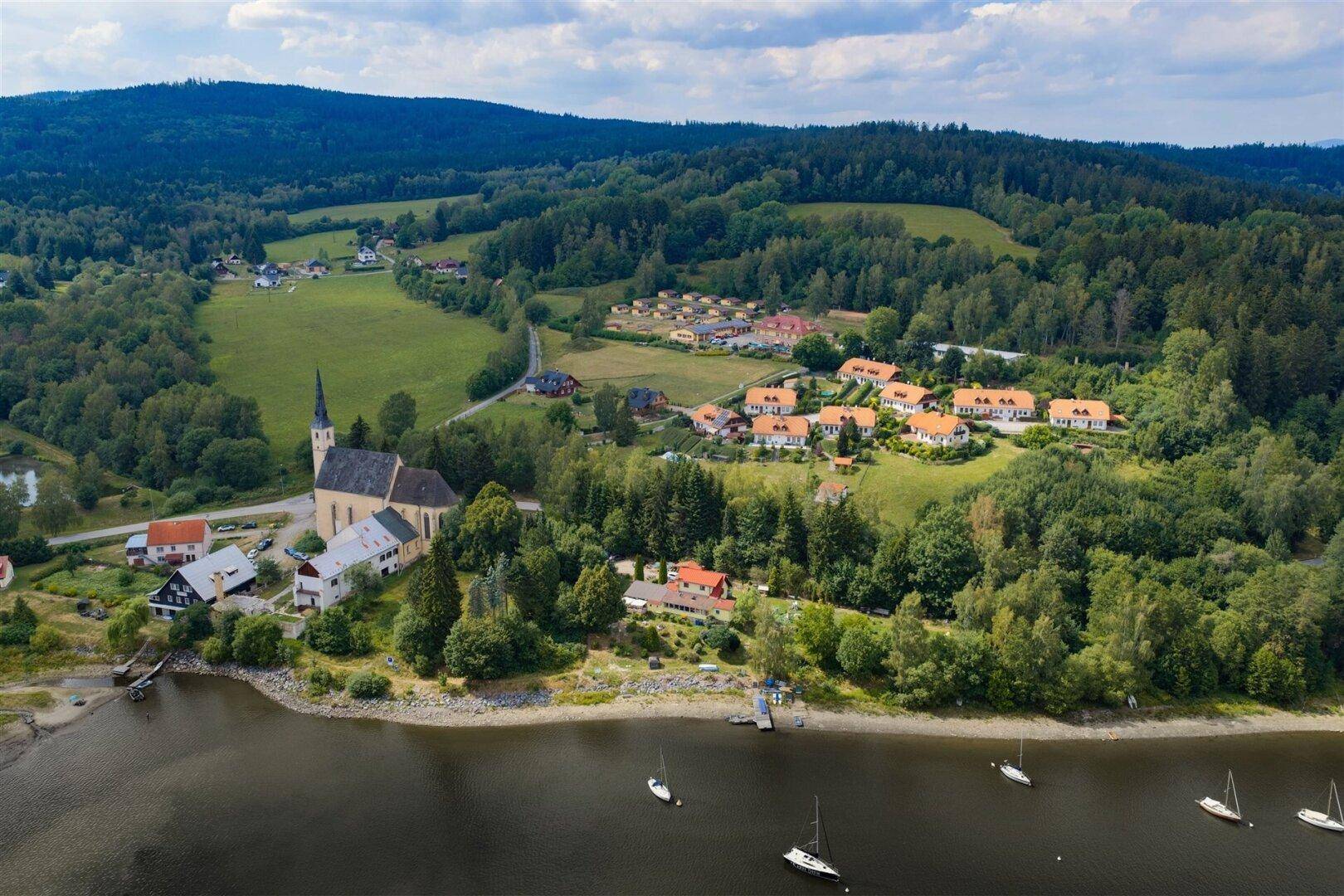 Malerische Luftaufnahme eines Dorfes am Seeufer mit Kirche und grüner Landschaft.