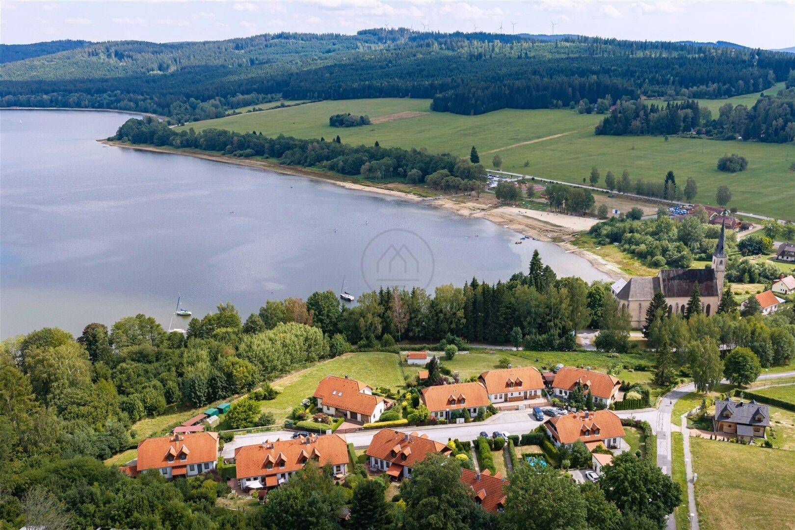 Panoramische Luftaufnahme eines malerischen Dorfes am See, eingebettet in eine grüne Waldlandschaft.