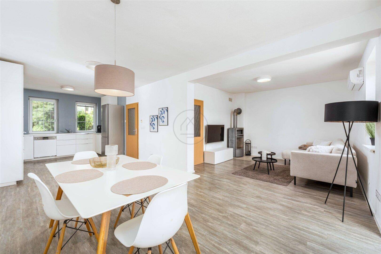 Offener Wohn-Essbereich mit integrierter Küche, modernem Esstisch und gemütlichem Sofa mit Kaminofen.