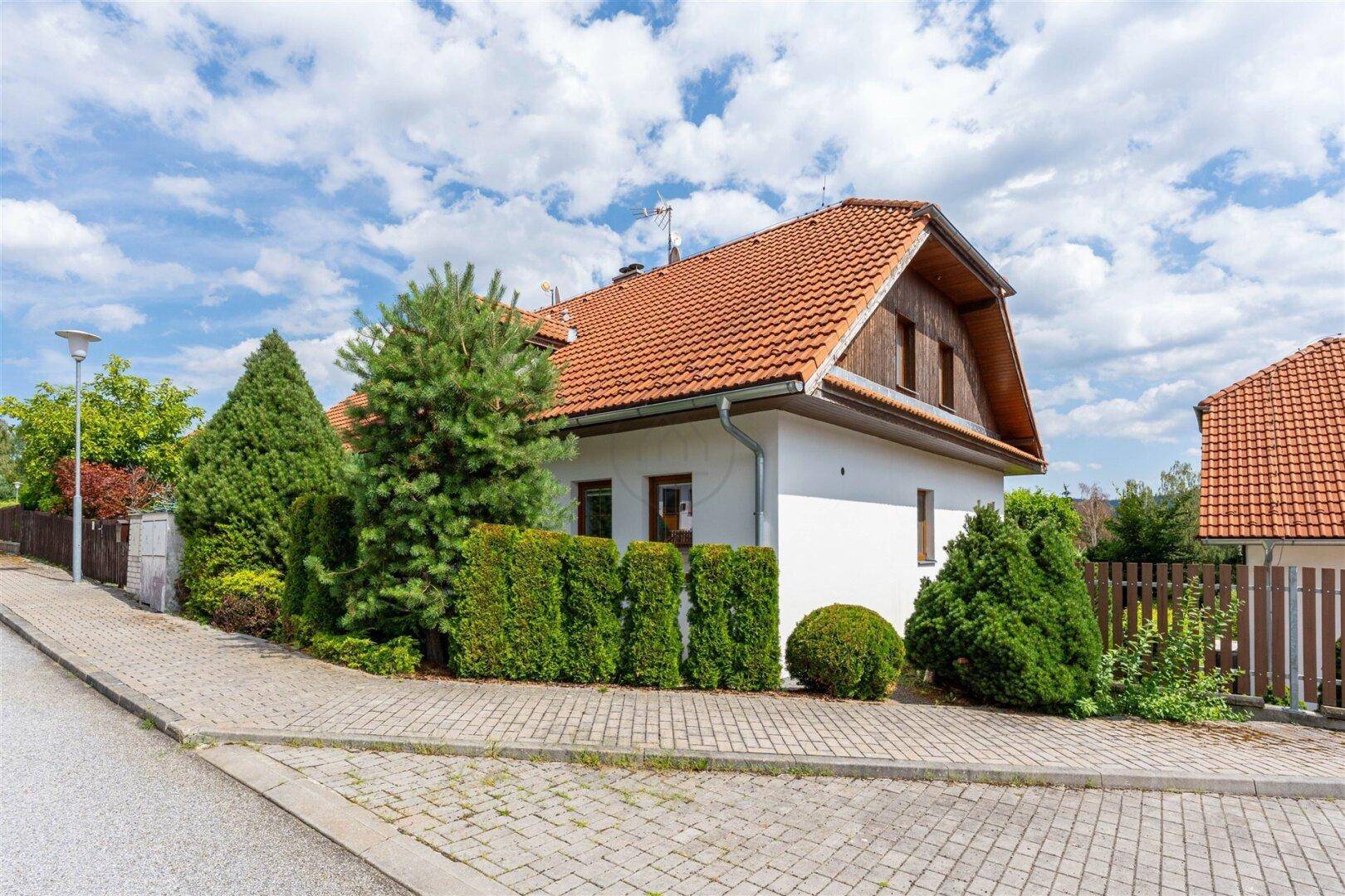 Ansicht des Hauses von der Straße mit gepflegtem Vorgarten und Hecke unter blauem Himmel.