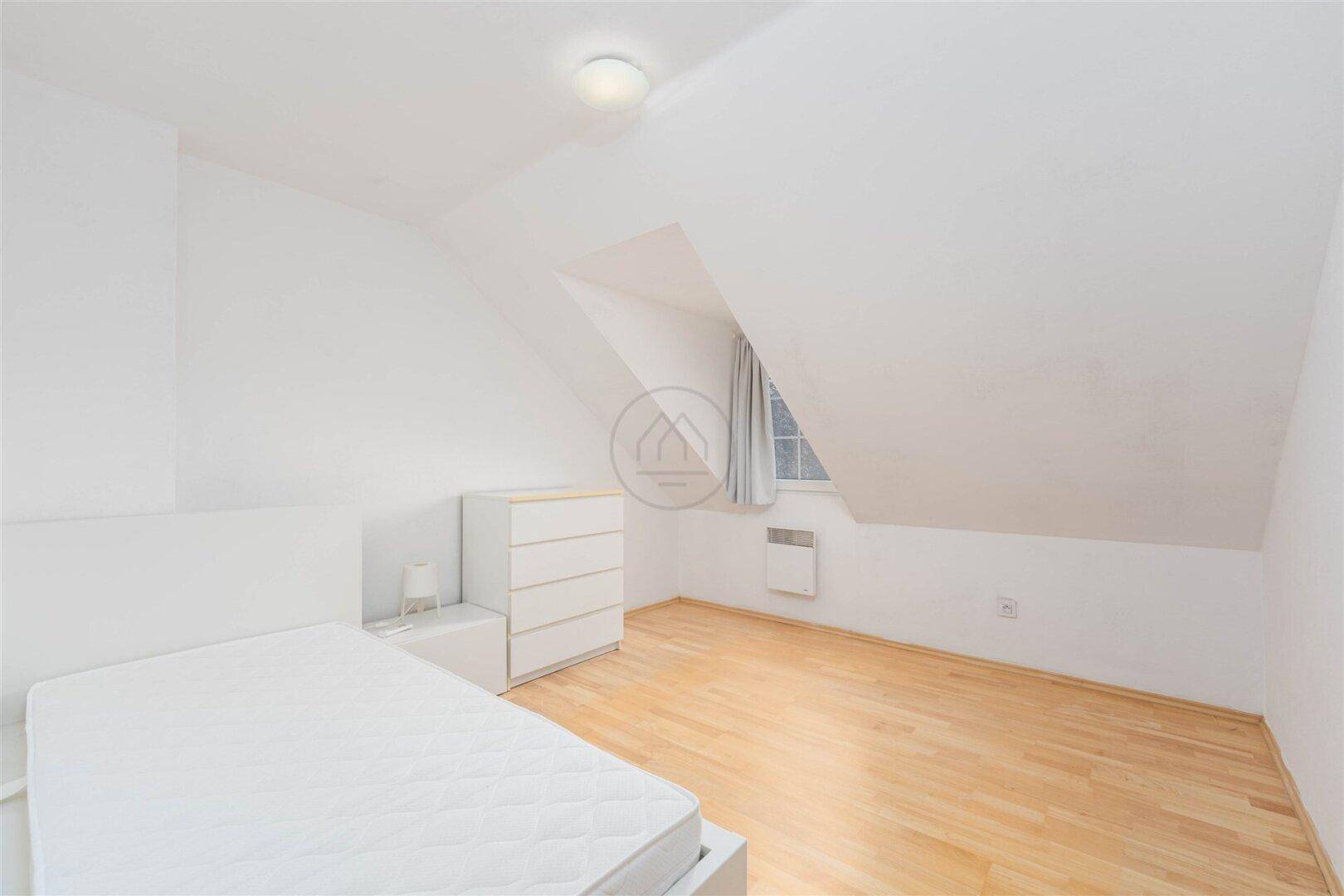 Helles Schlafzimmer im Dachgeschoss mit Dachschräge, Holzboden und minimalistischer Einrichtung.
