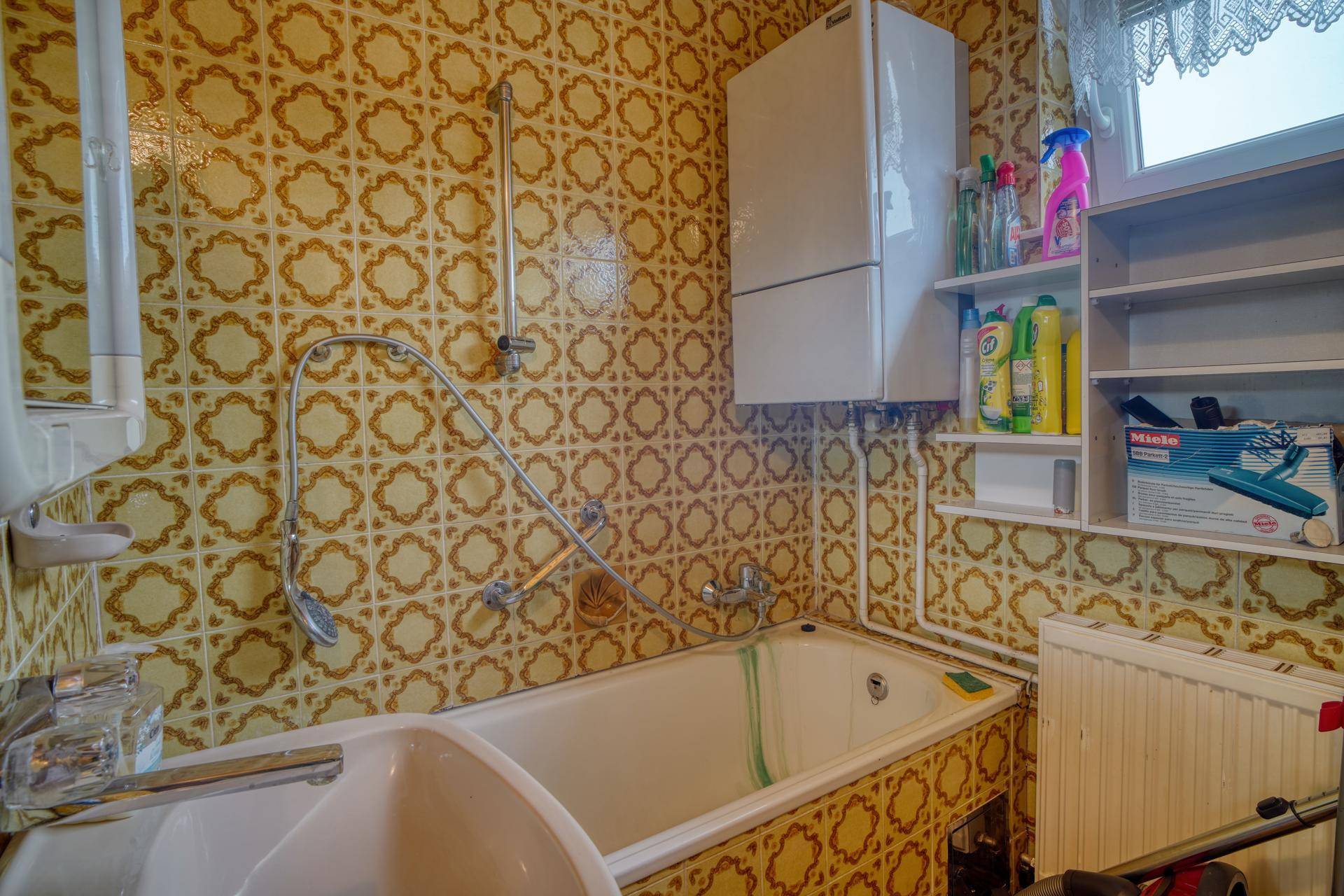 Badezimmer mit Badewanne, Waschbecken und auffälligen gelb-braunen Fliesen im Retro-Stil.