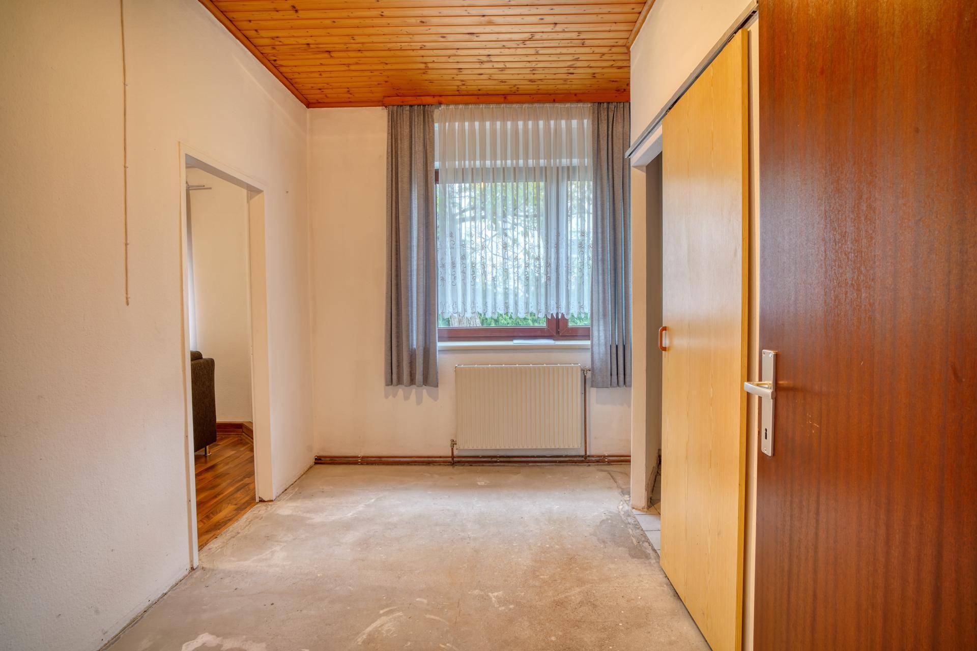 Leerer Raum mit Holzdecke, Fenster und Heizkörper, bereit für neue Gestaltungsideen.