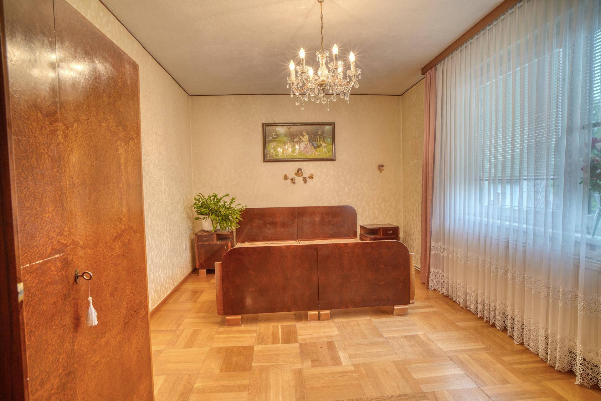 Schlafzimmer mit Parkettboden, Doppelbett und einem Kronleuchter an der Decke.