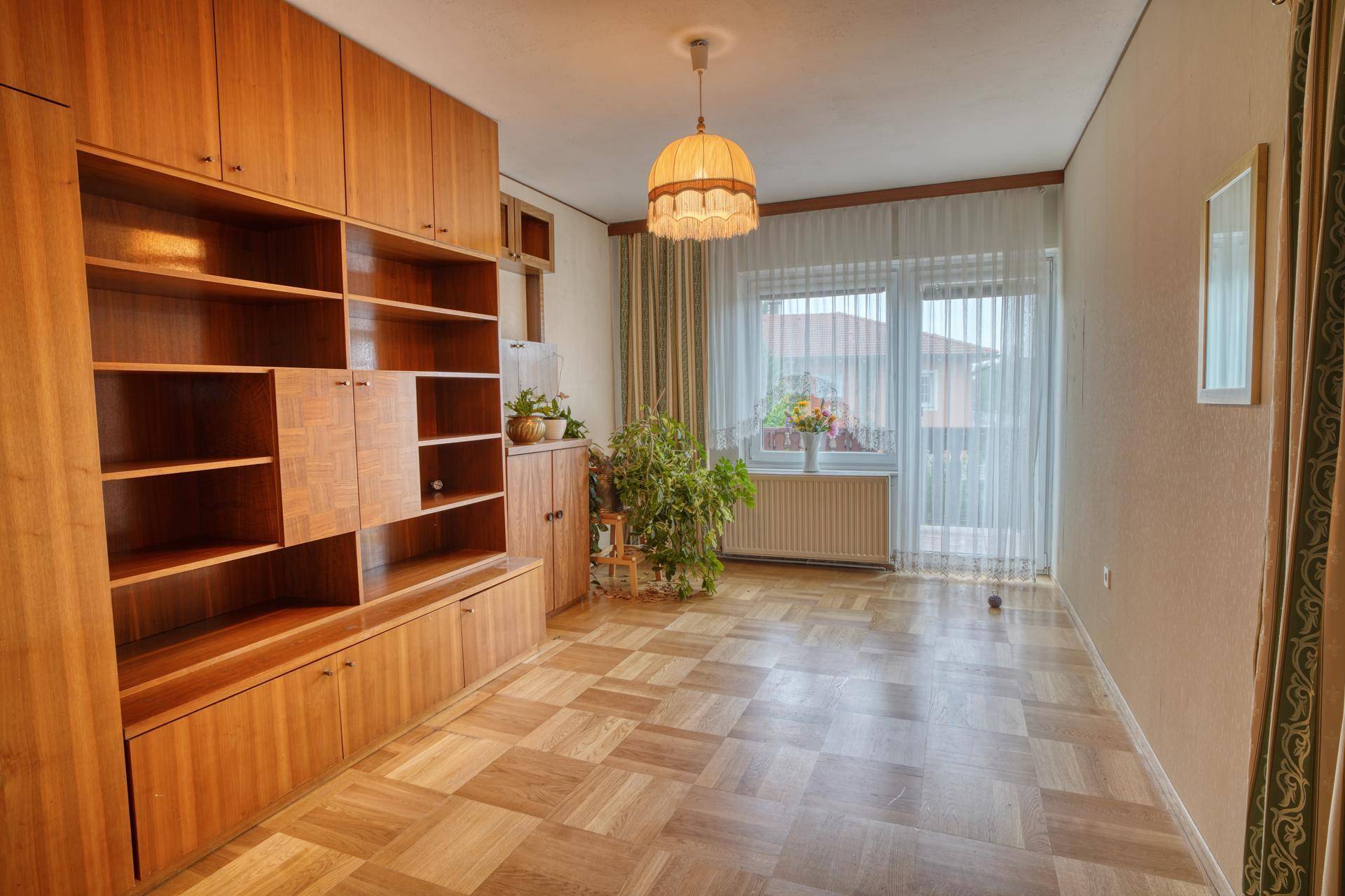 Zimmer mit Parkettboden, großem Holzregal und Fenster mit Blick nach draußen.