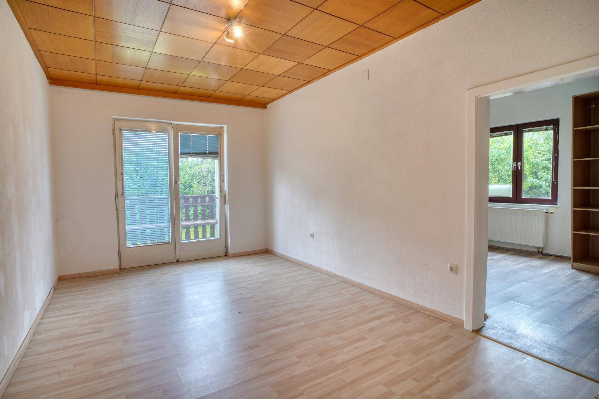 Heller Raum mit Holzboden, Holzdecke und Zugang zu einem Balkon.