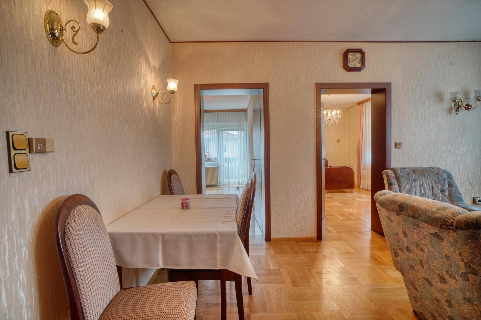 Essbereich mit Holztisch und Stühlen, angrenzend an einen Wohnbereich mit Parkettboden.