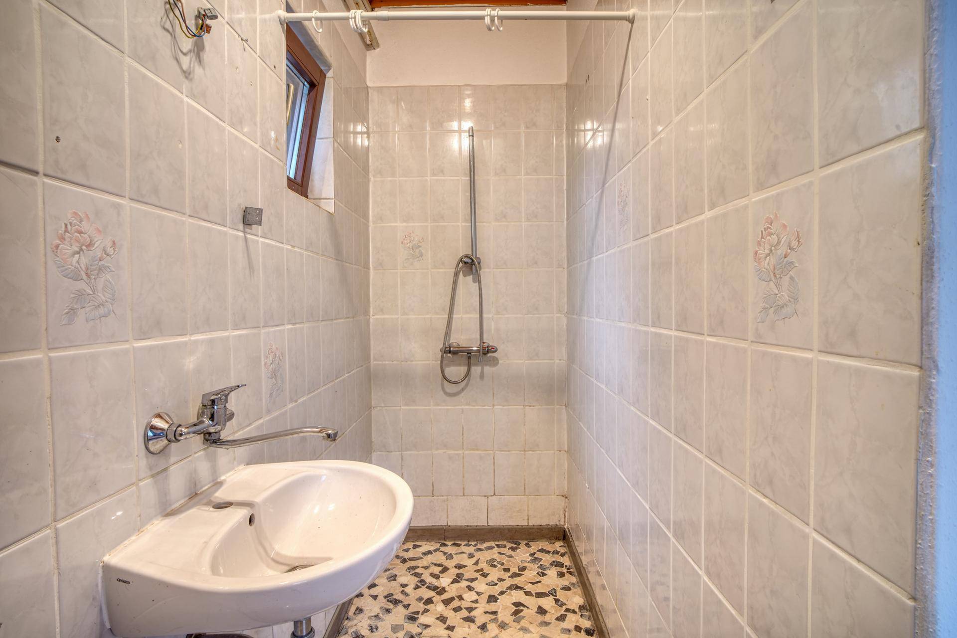 Kleines Badezimmer mit Duschbereich, Waschbecken und hellen Fliesen an den Wänden.