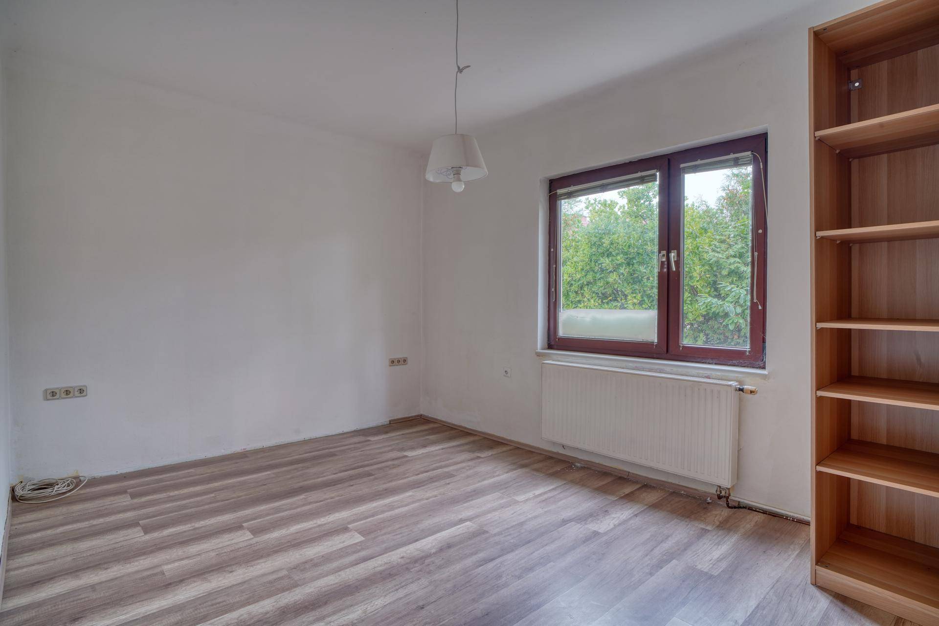 Schlafzimmer mit Laminatboden, Fenster und einem Bücherregal an der Wand.