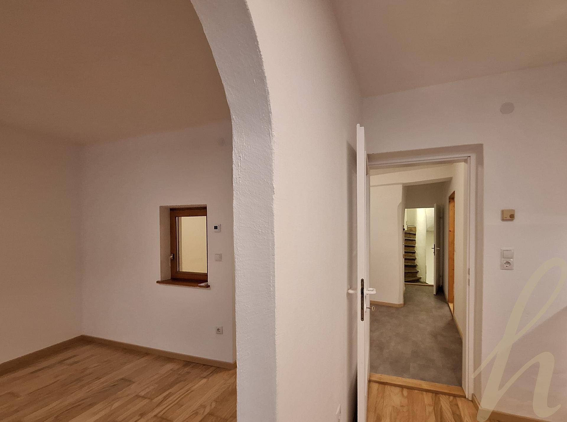 Heller Innenraum mit einem eleganten Rundbogen und Blick in einen angrenzenden Bereich mit Treppe.