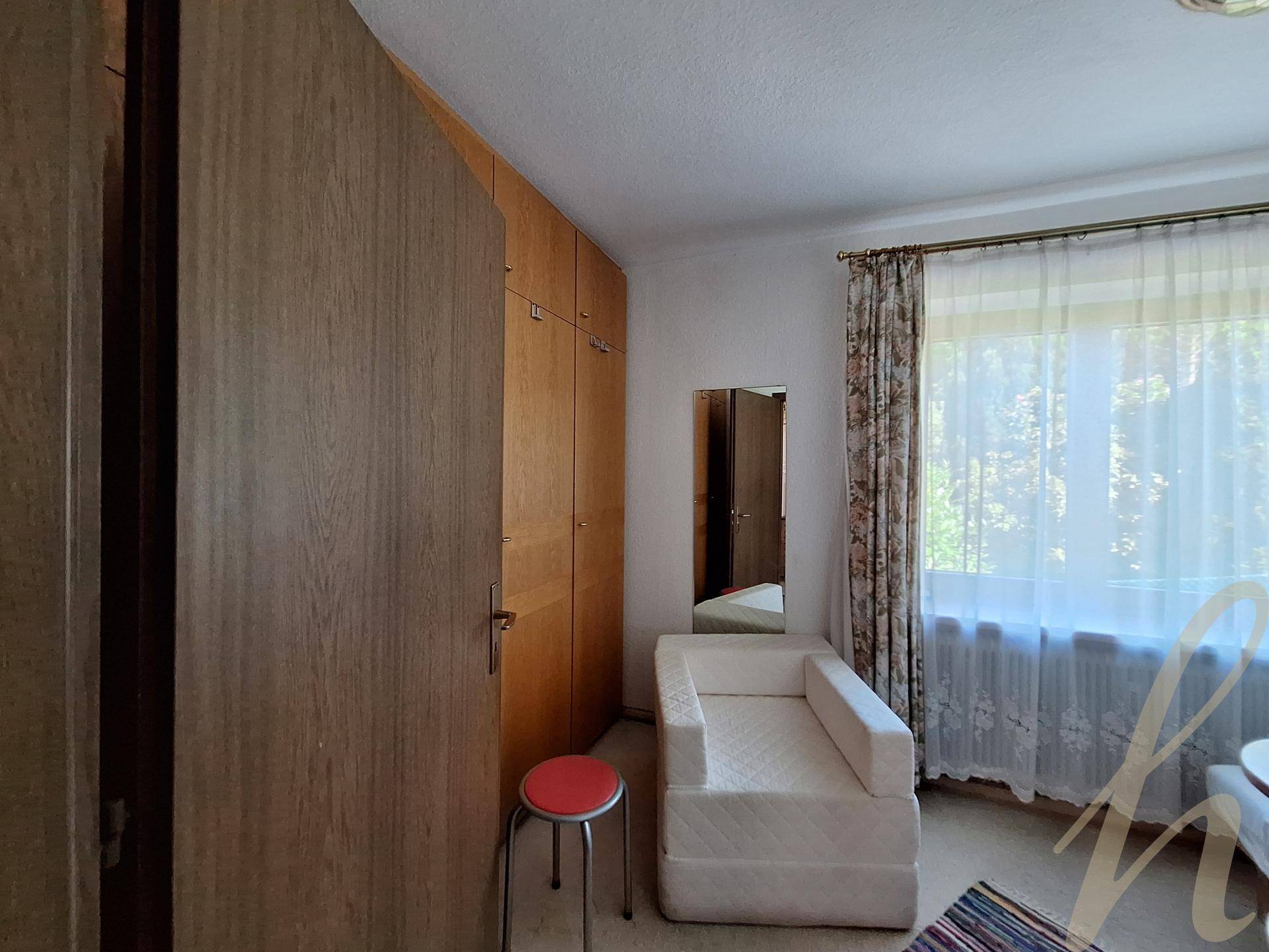 Schlafzimmer mit Einbauschränken, kleinem Sofa und Fenster mit Blick ins Grüne.