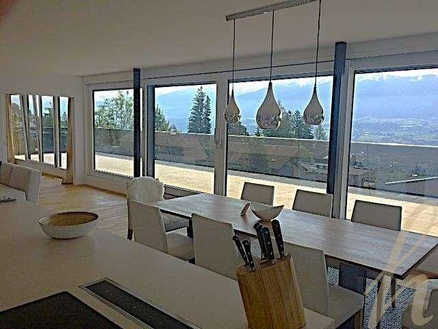 Essbereich mit großem Tisch und raumhohen Fenstern, die einen weiten Blick auf die Berge und das Tal bieten.