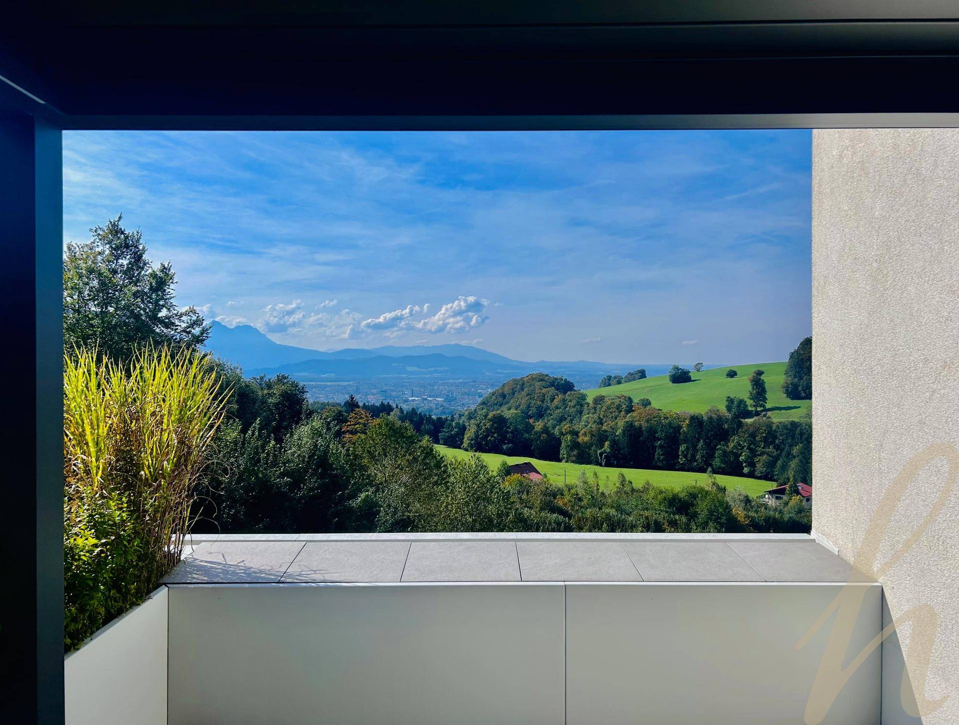 Panoramablick von einem Balkon auf die umliegende grüne Landschaft und ferne Berge.