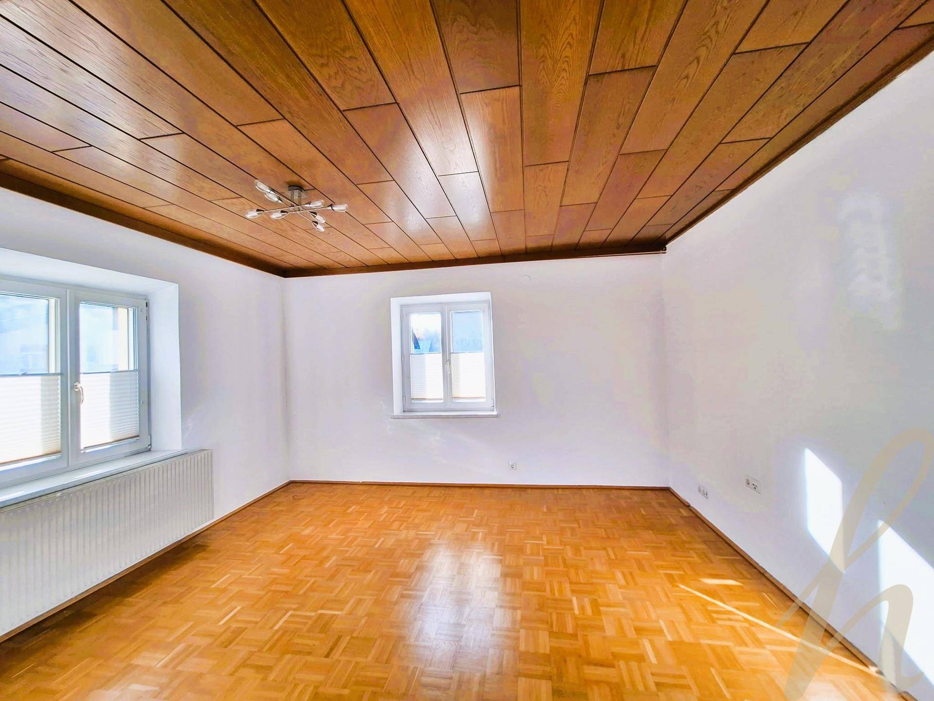 Heller Raum mit Parkettboden, weiß gestrichenen Wänden und einer Holzdeckenverkleidung.