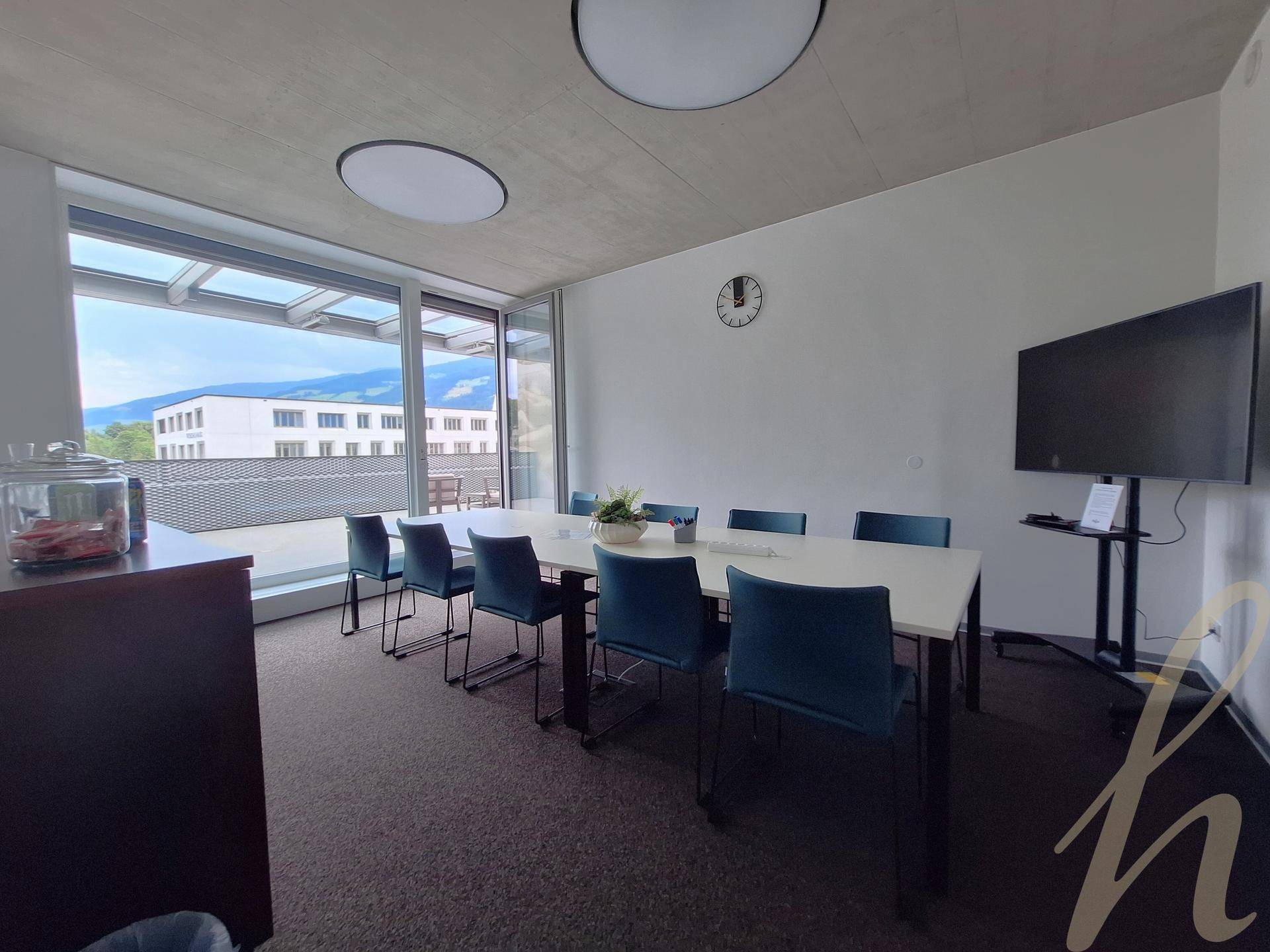 Heller Konferenzraum mit Teppichboden, modernen Möbeln und Zugang zu einer Außenterrasse mit Bergblick.